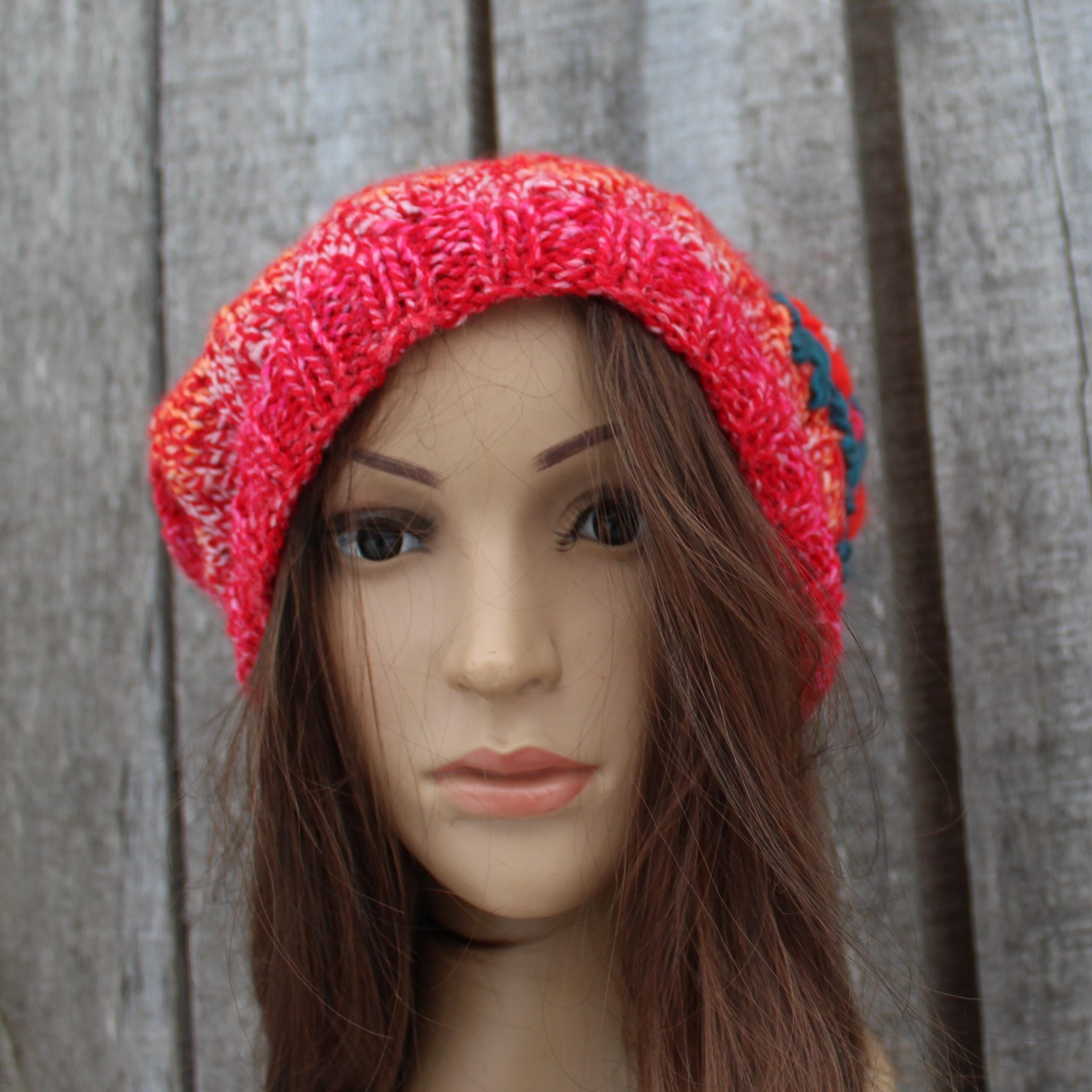 Mannequin head wearing a red knitted hat against a wooden background