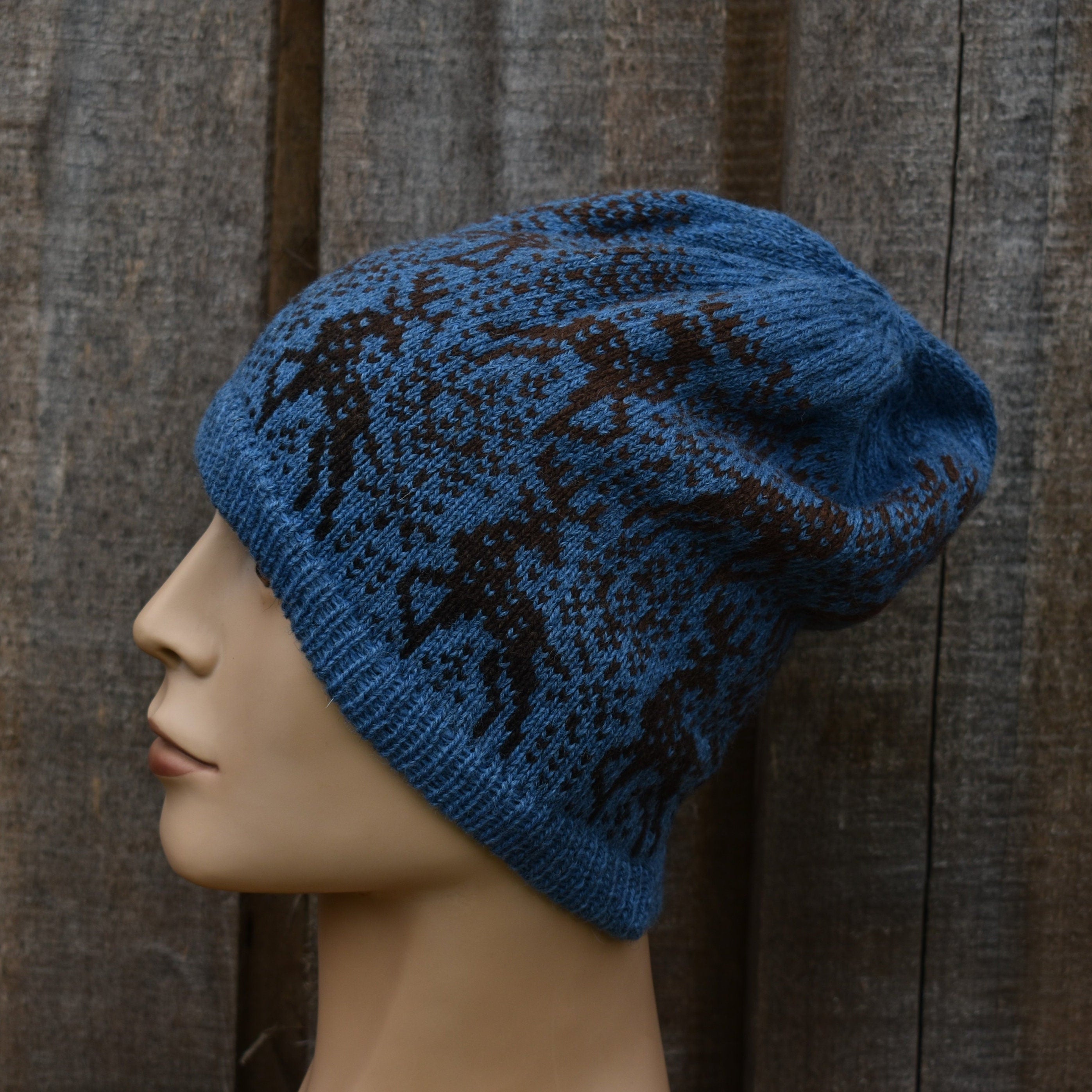 Blue knitted hat with black patterns on a mannequin head against a wooden background