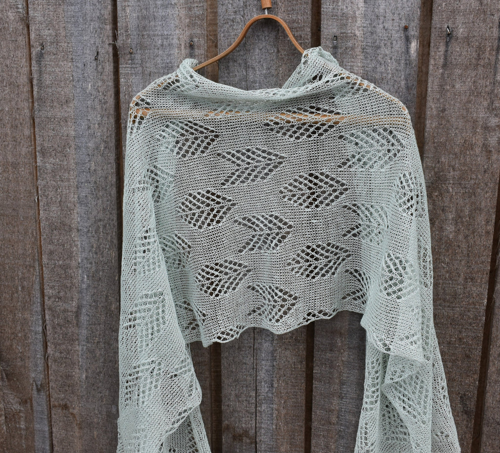 Knitted shawl with a geometric pattern hanging on a wooden hook against a wooden background