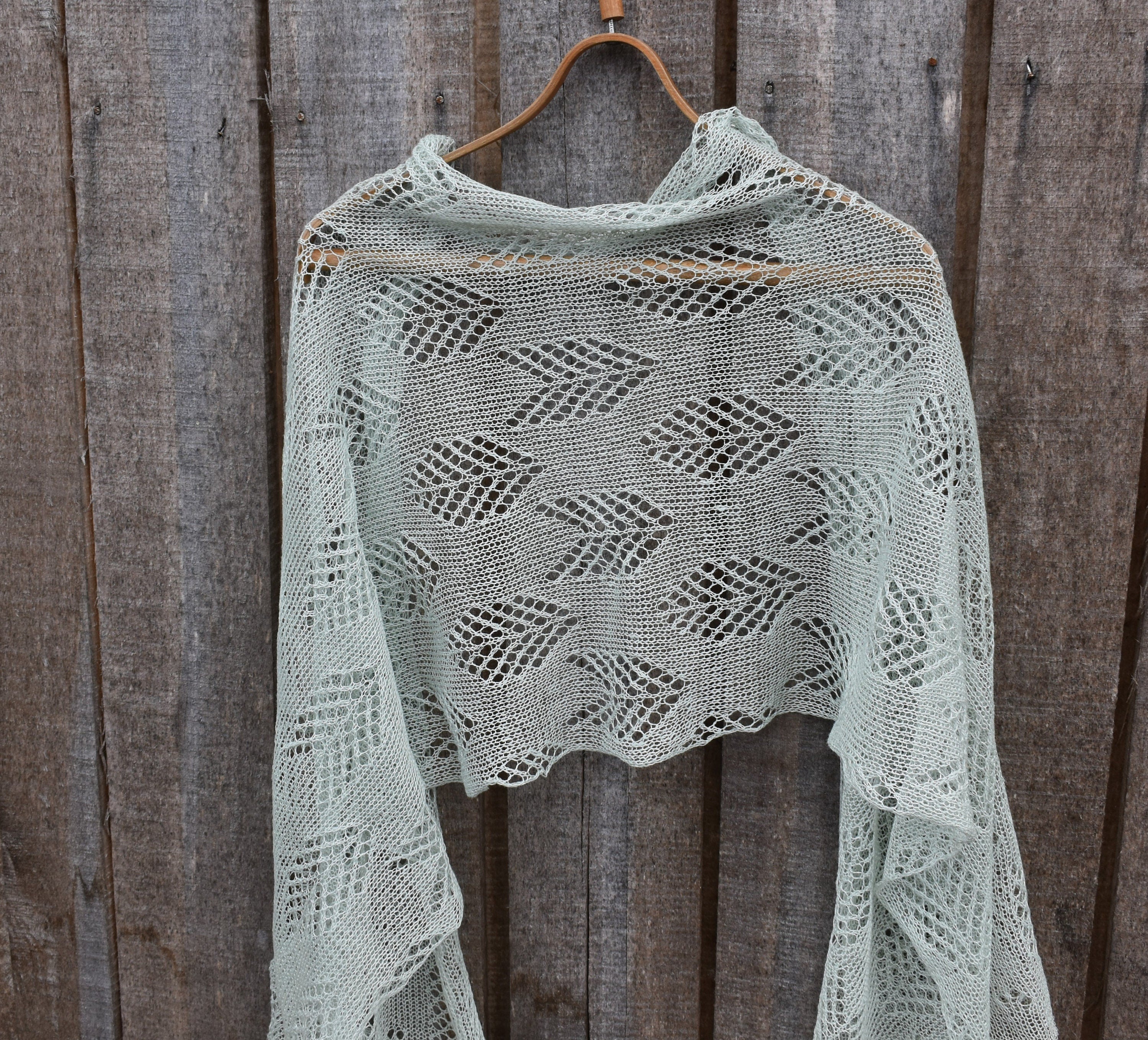 Knitted shawl with a geometric pattern hanging on a wooden hook against a wooden background
