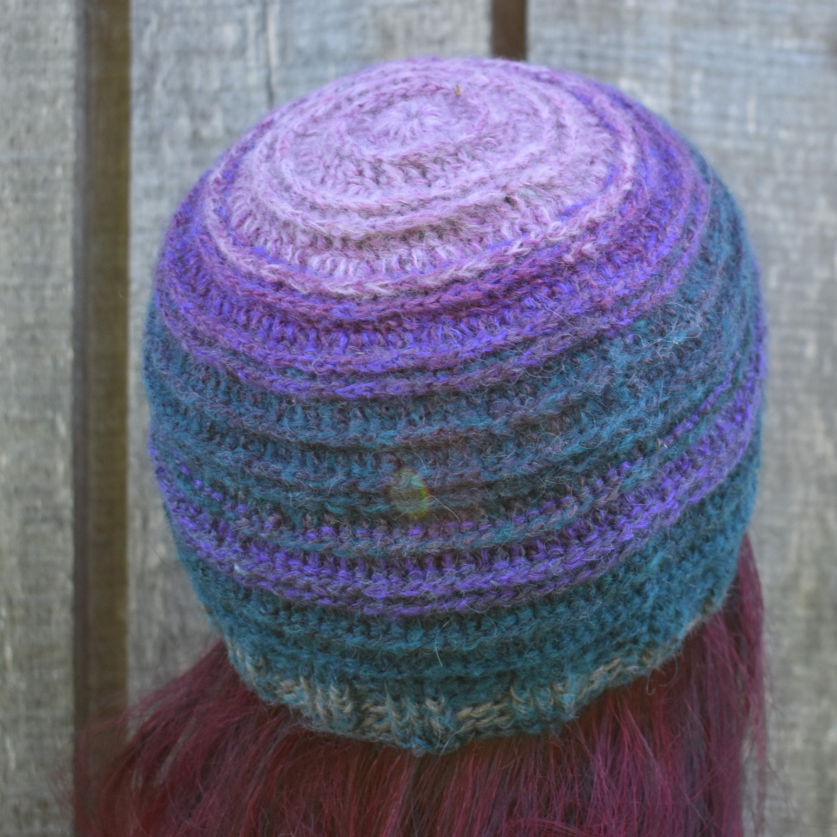 Multicolored knitted beanie on a person with pink hair against a wooden fence background