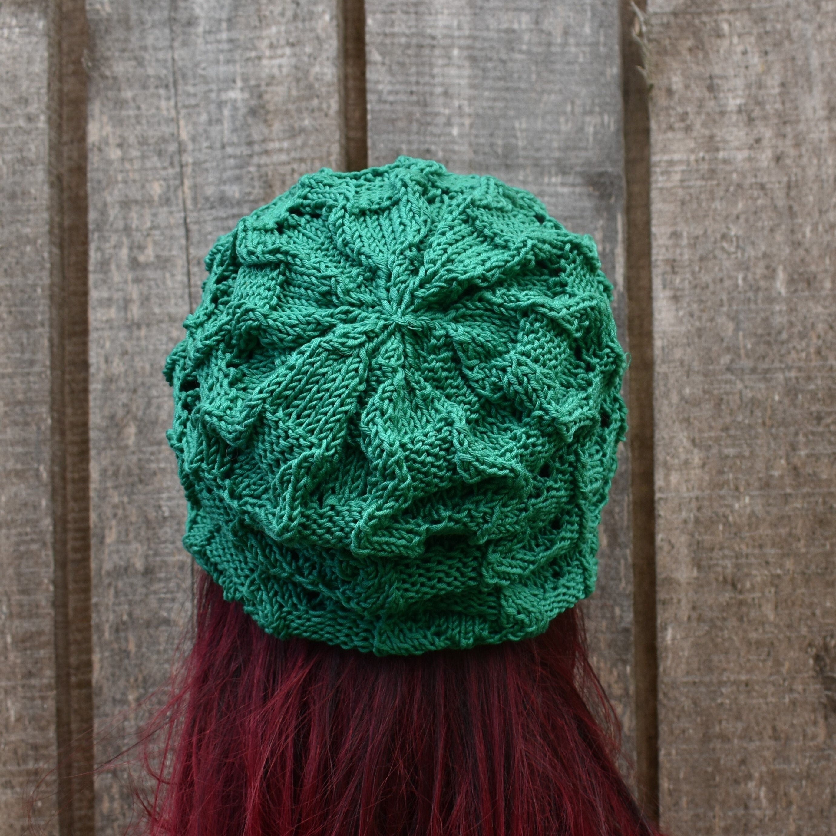 Green knitted hat on a person with red hair against a wooden background