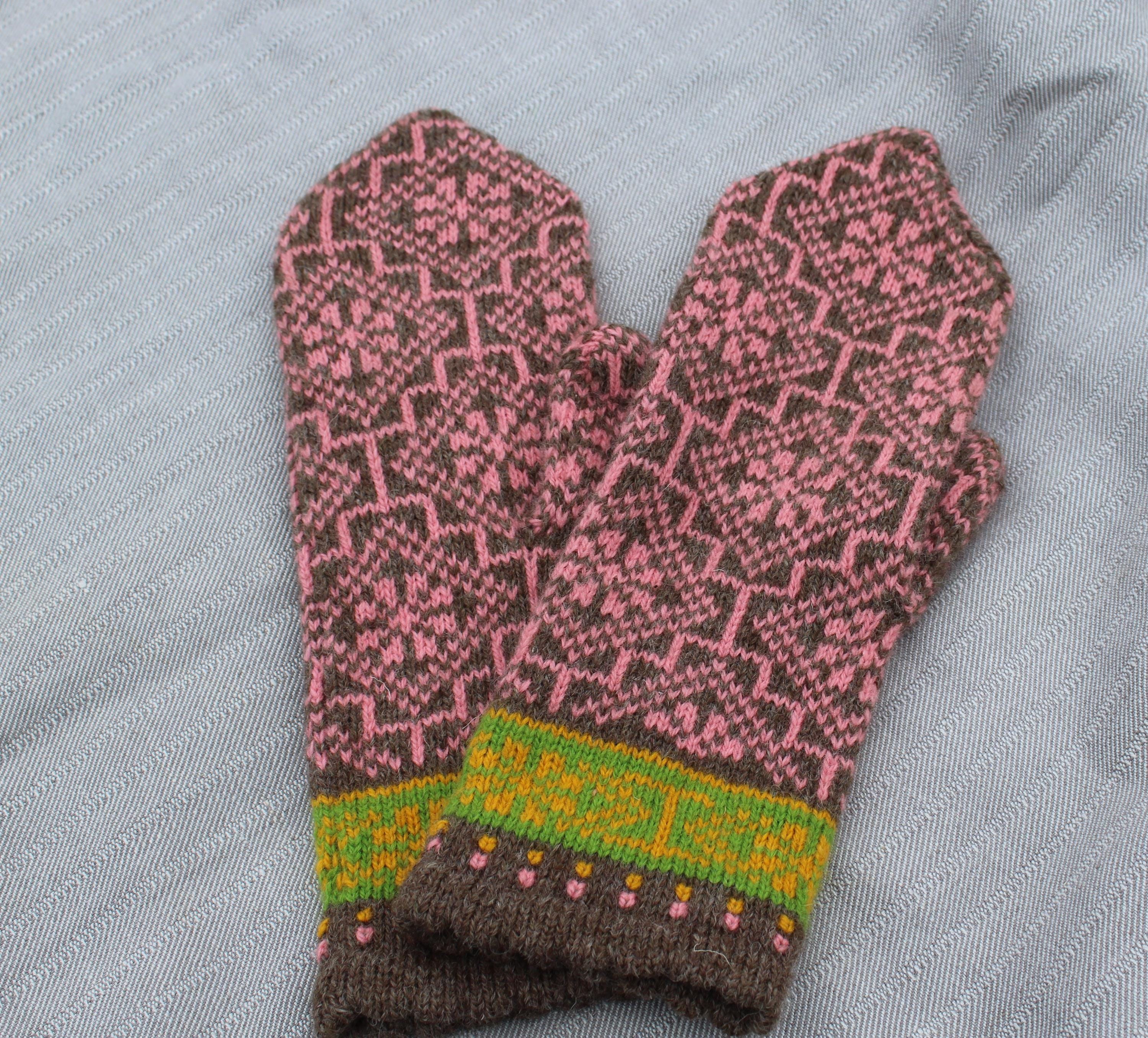 Knitted mittens with a pink and brown pattern on a gray fabric background
