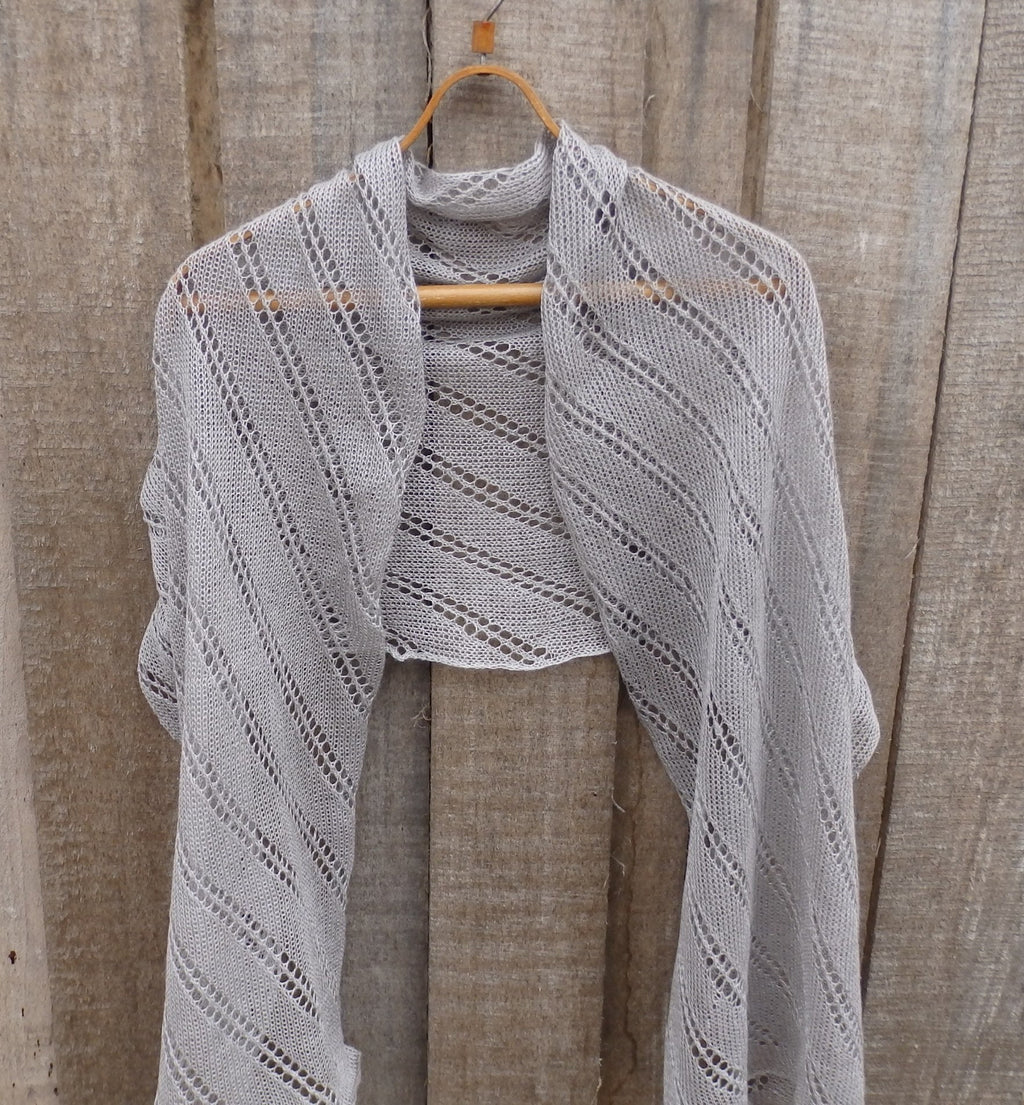 Gray knitted shawl on a wooden hanger against a wooden background