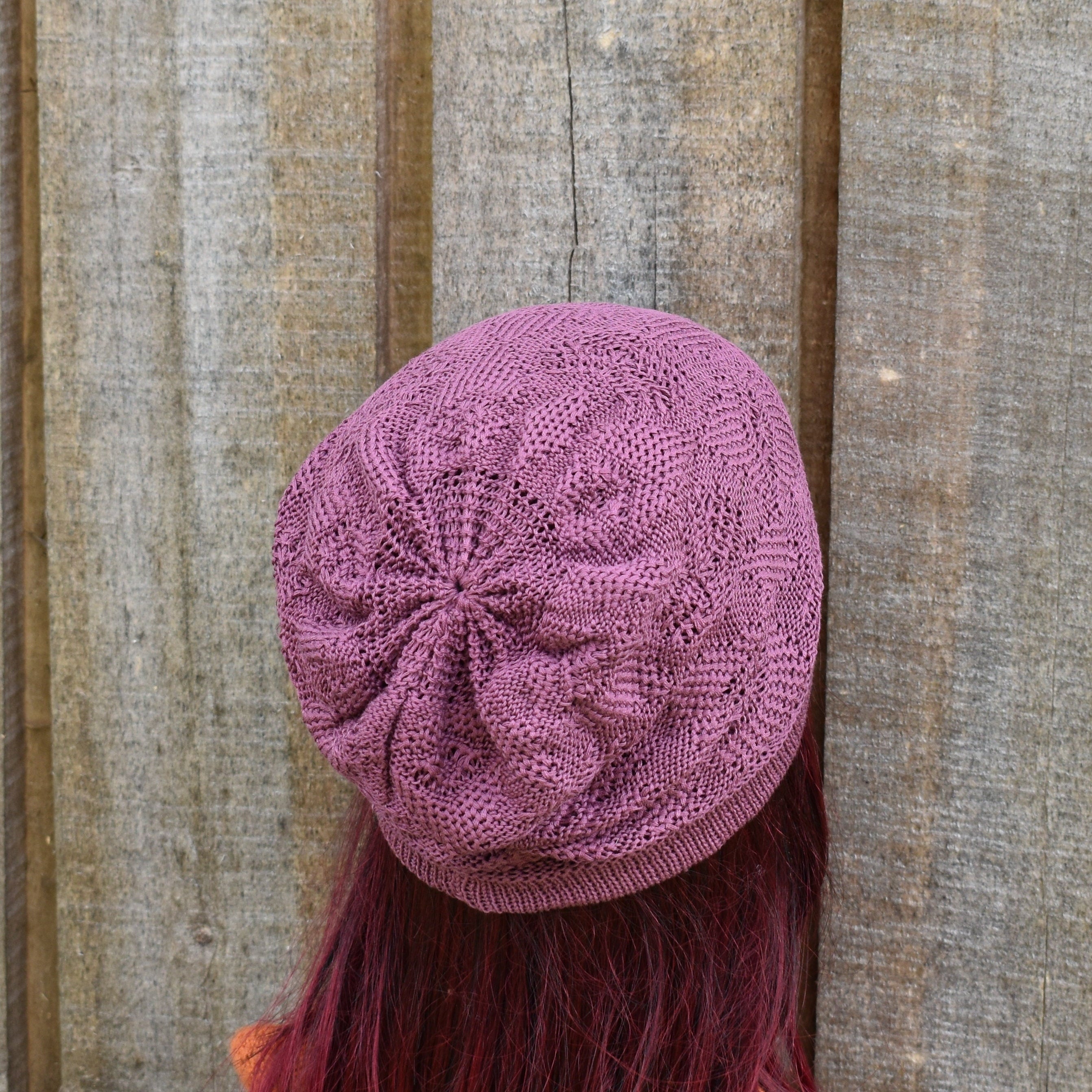 Purple knitted beanie on a person with red hair against a wooden background