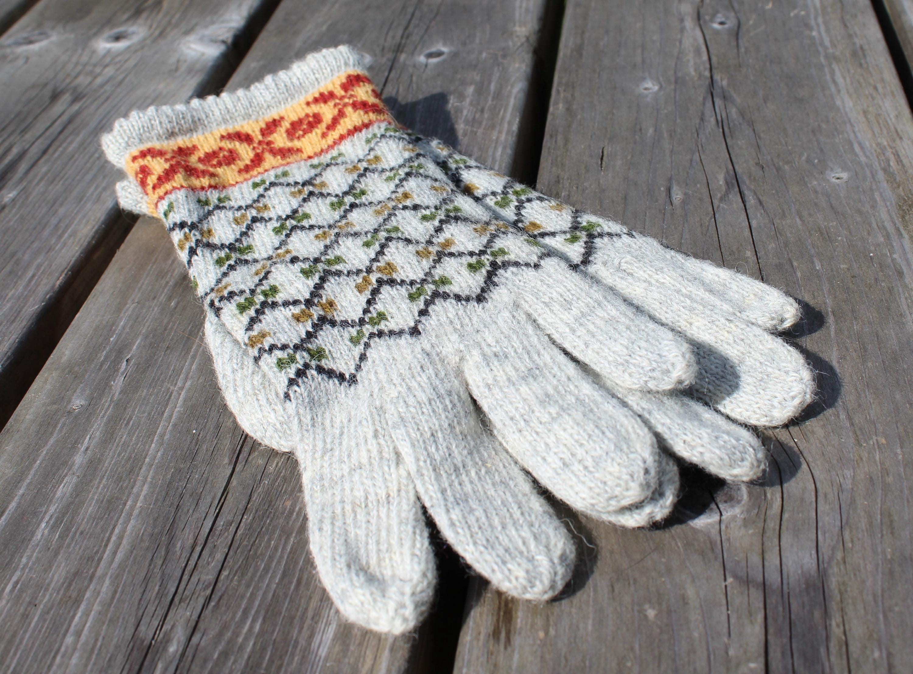 Pair of white gloves with patterned cuffs on a wooden surface