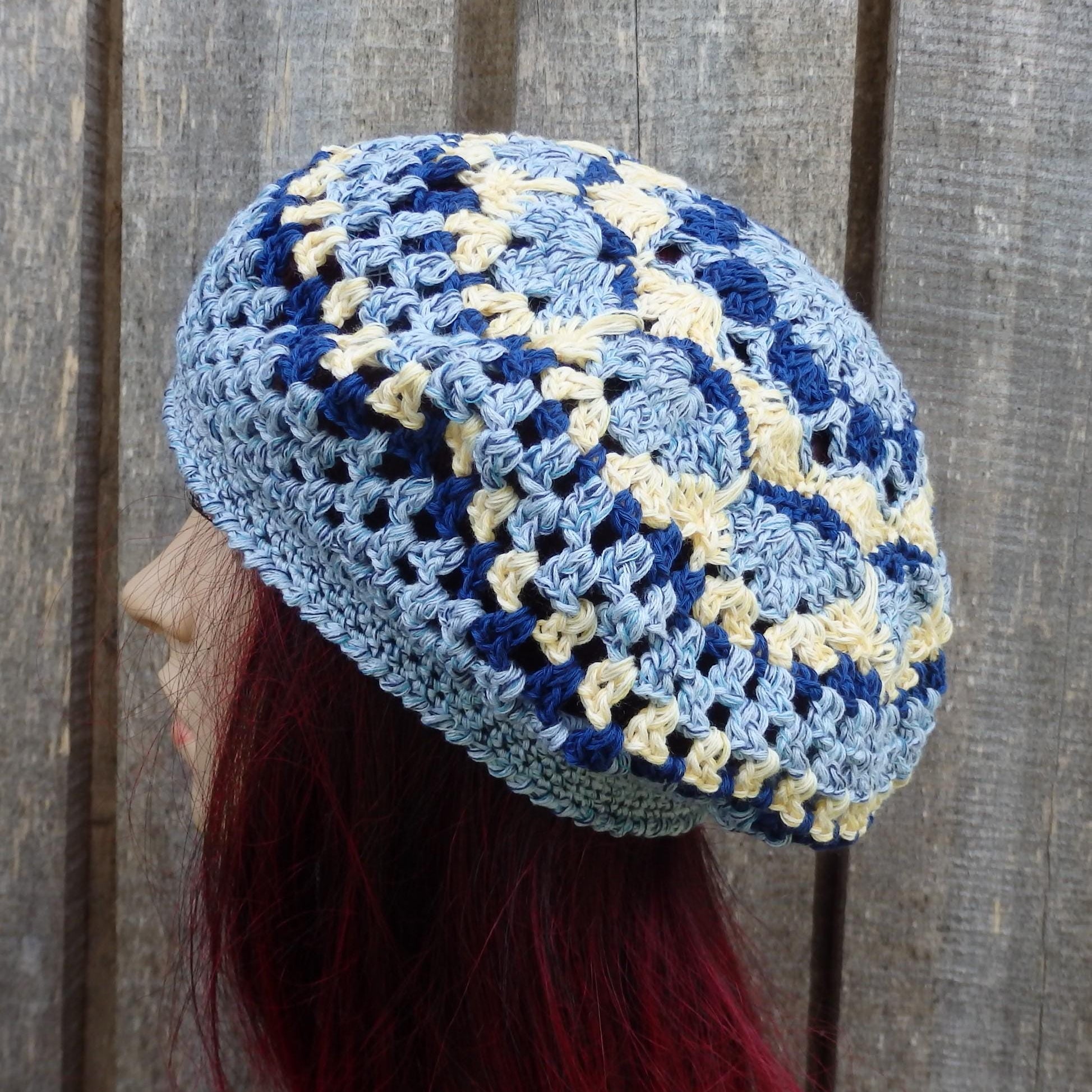 Blue and yellow crocheted beanie worn by a person with red hair against a wooden background