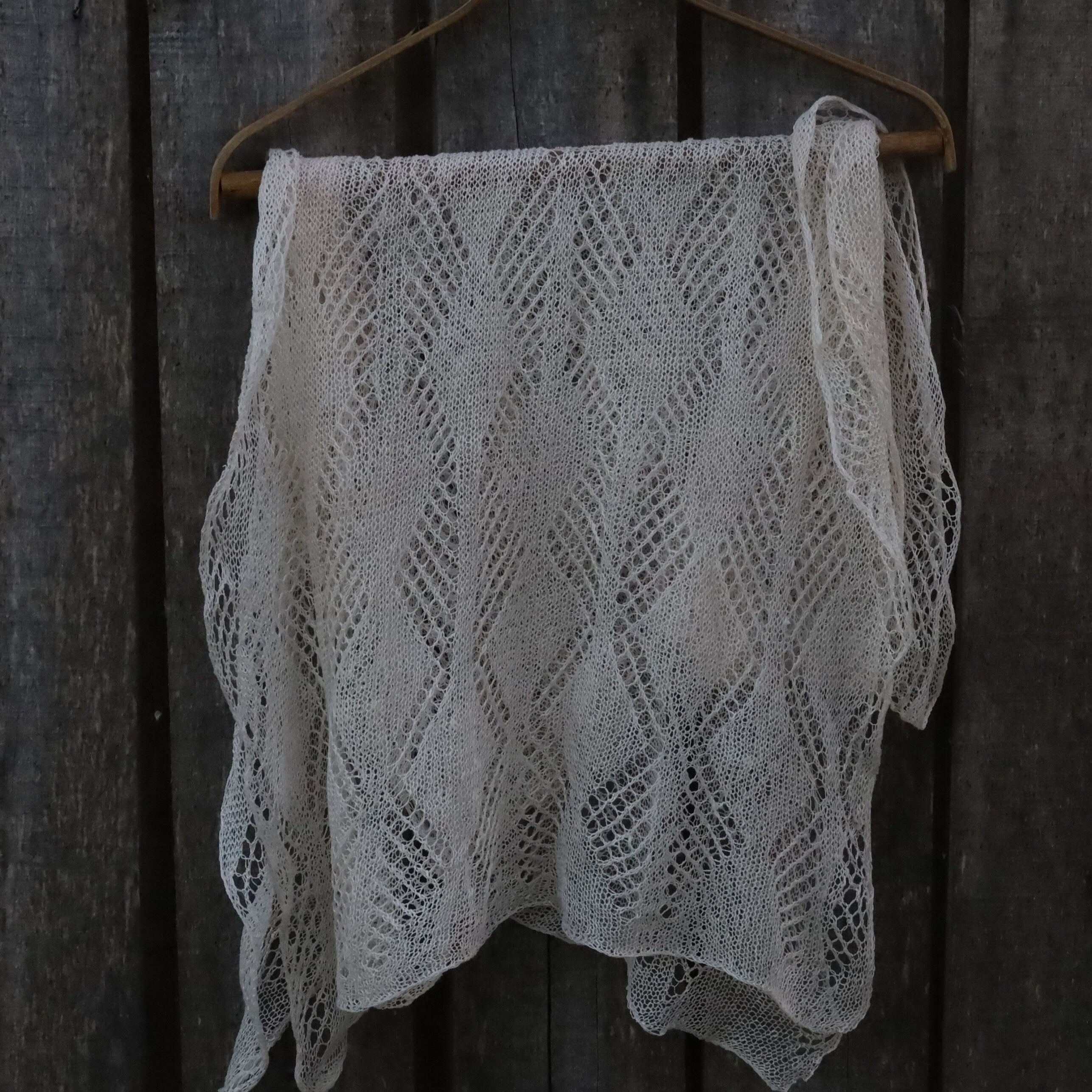 Knitted shawl with a geometric pattern hanging on a wooden hanger against a wooden background