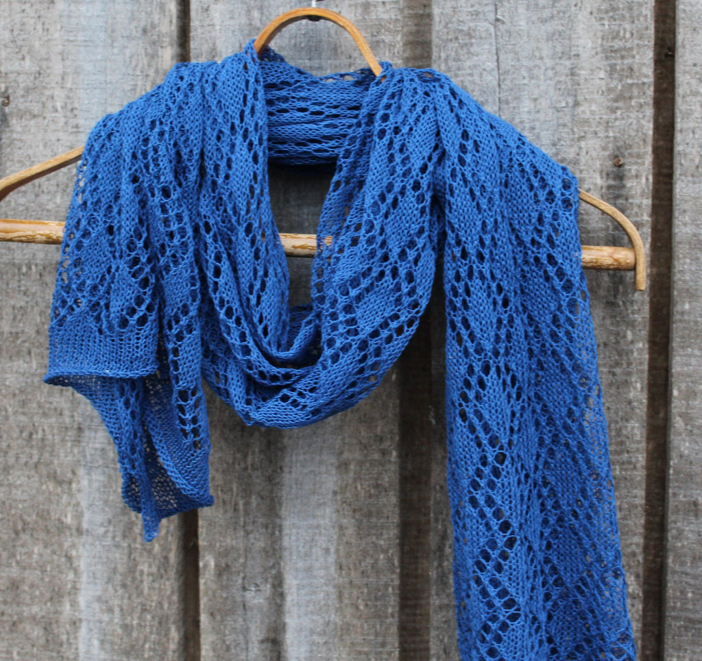 Blue knitted shawl on a wooden hanger against a rustic wooden background