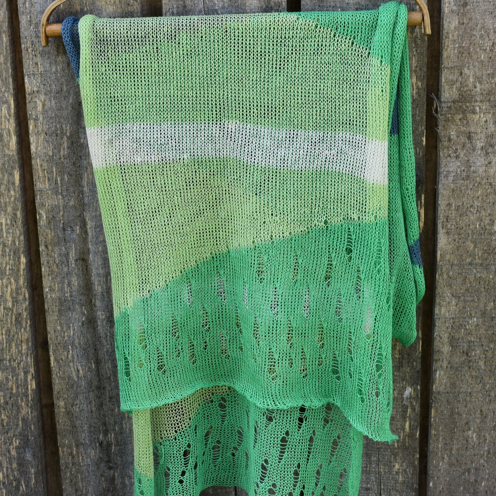 Green knitted shawl hanging on a wooden hook against a wooden background