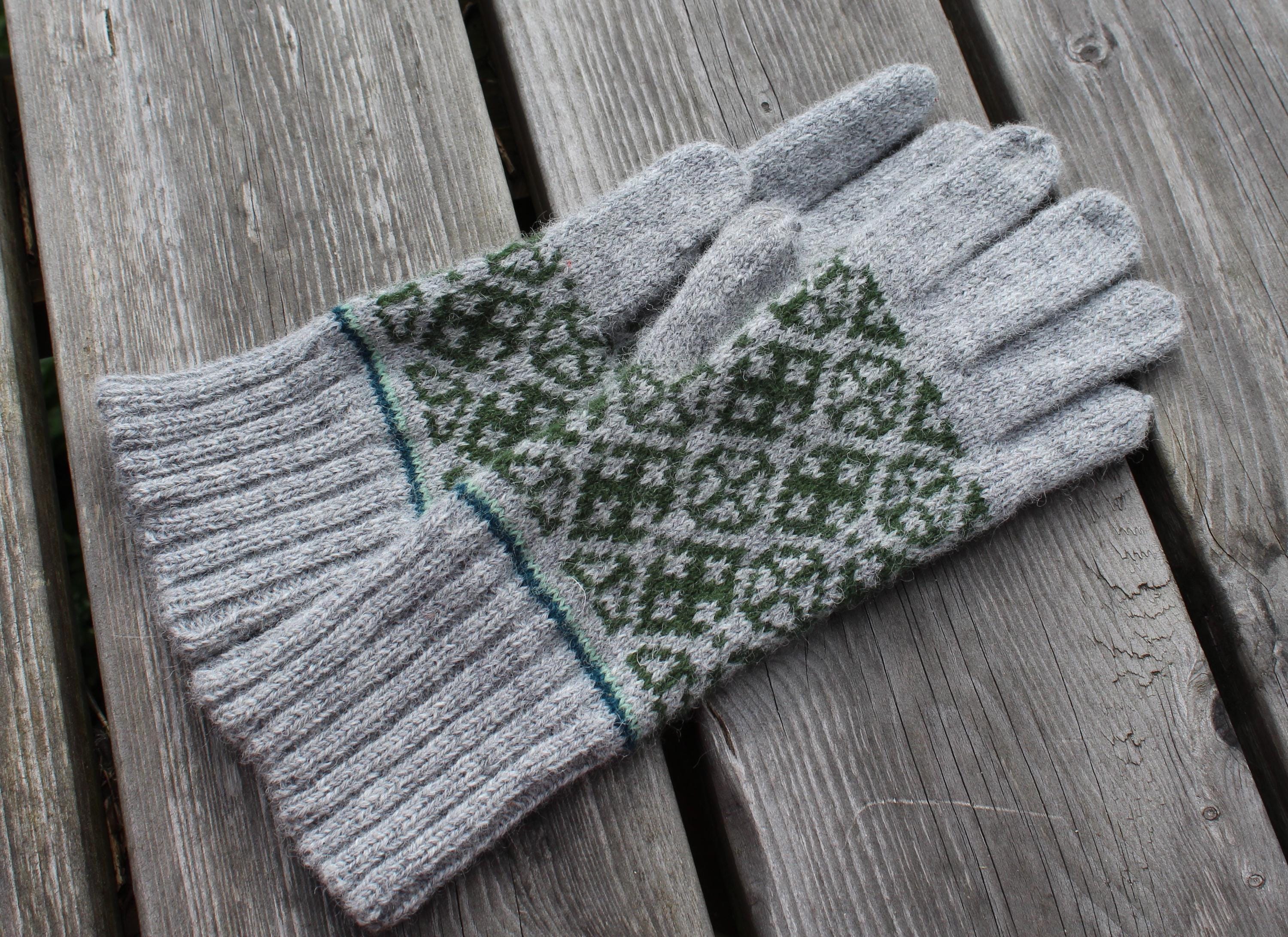 Pair of gray gloves with green pattern on a wooden surface