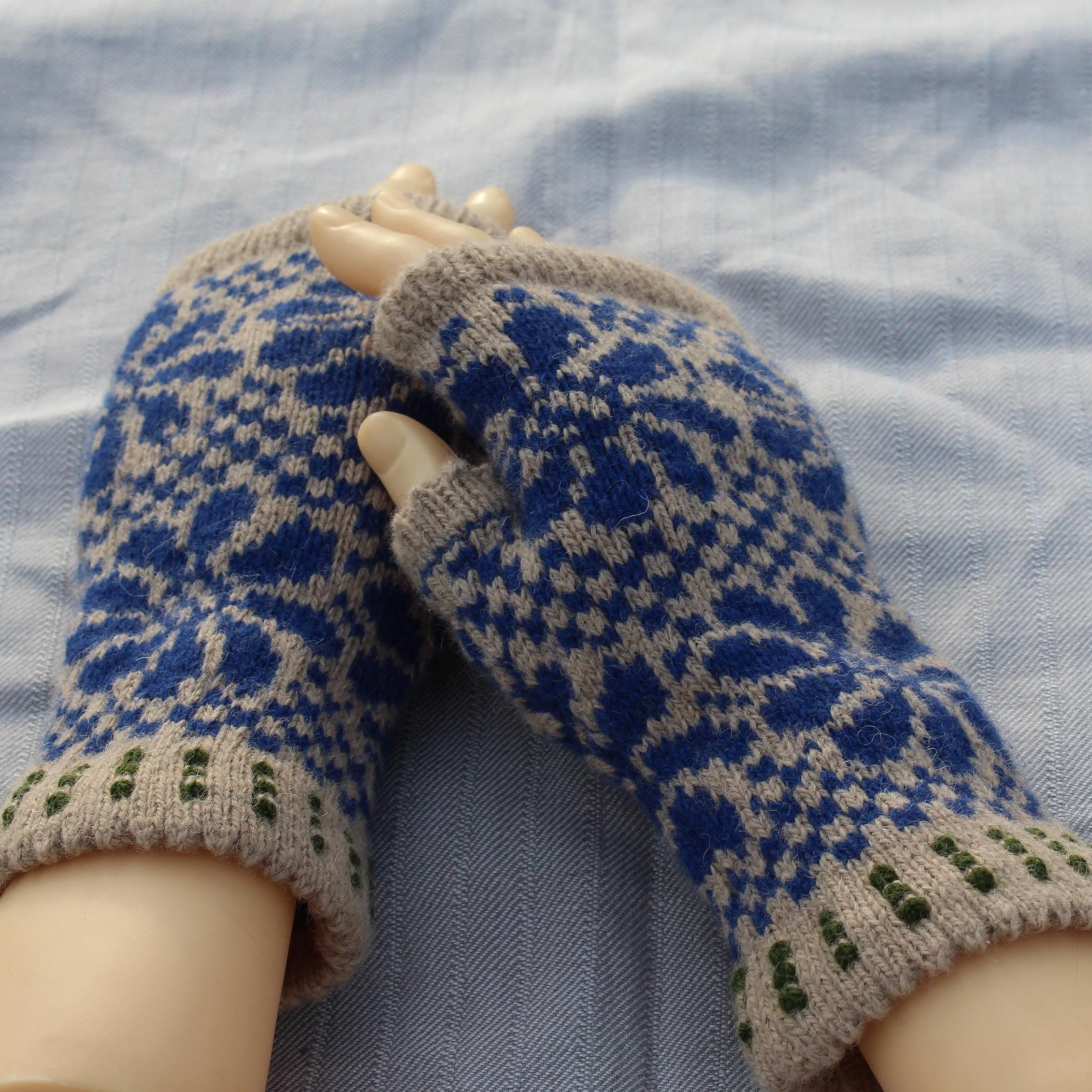 Pair of blue and beige patterned gloves on a mannequin hand against a textured fabric background