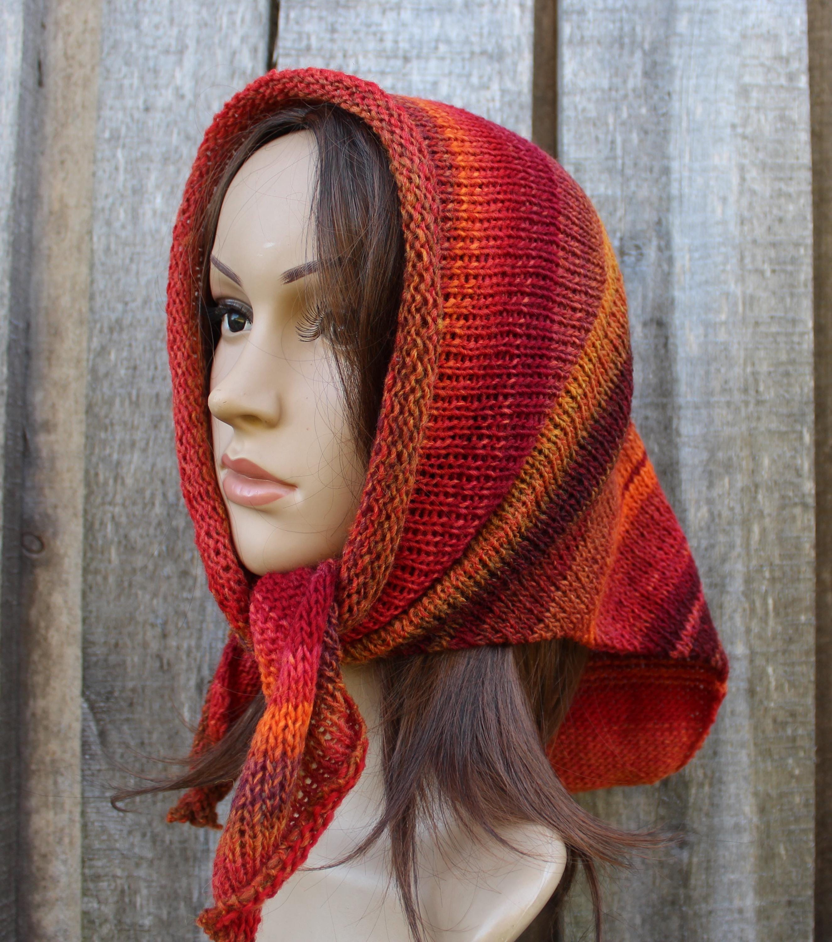 Mannequin head wearing a red and orange knitted head wrap against a wooden background