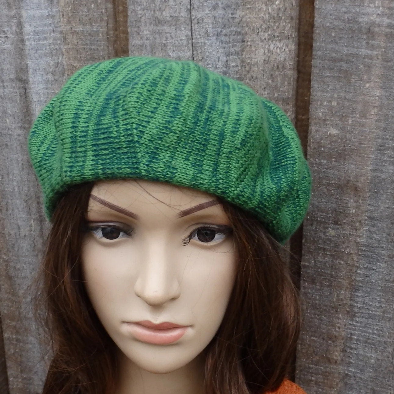 Green knitted beret on a mannequin head against a wooden background