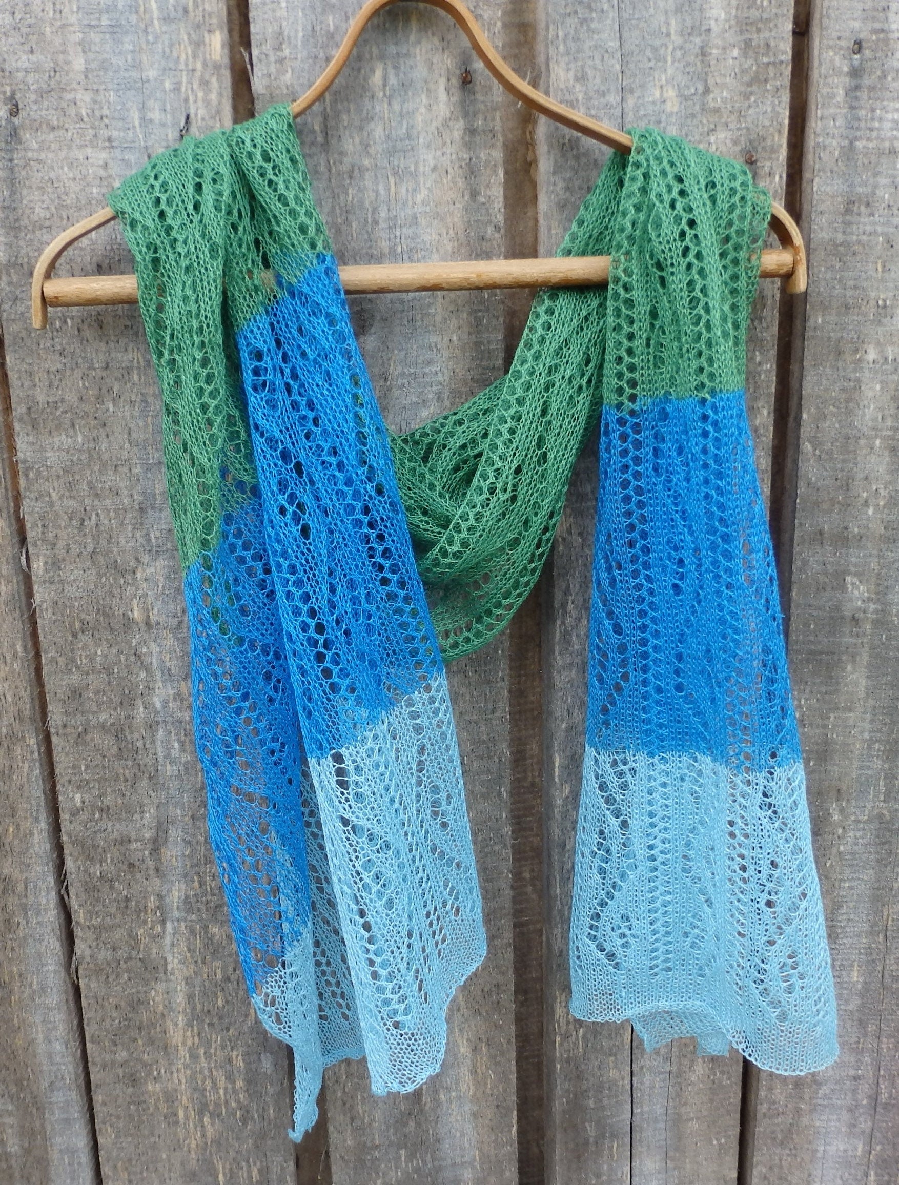 Knitted scarf with green, blue, and light blue gradient on a wooden hanger against a wooden background