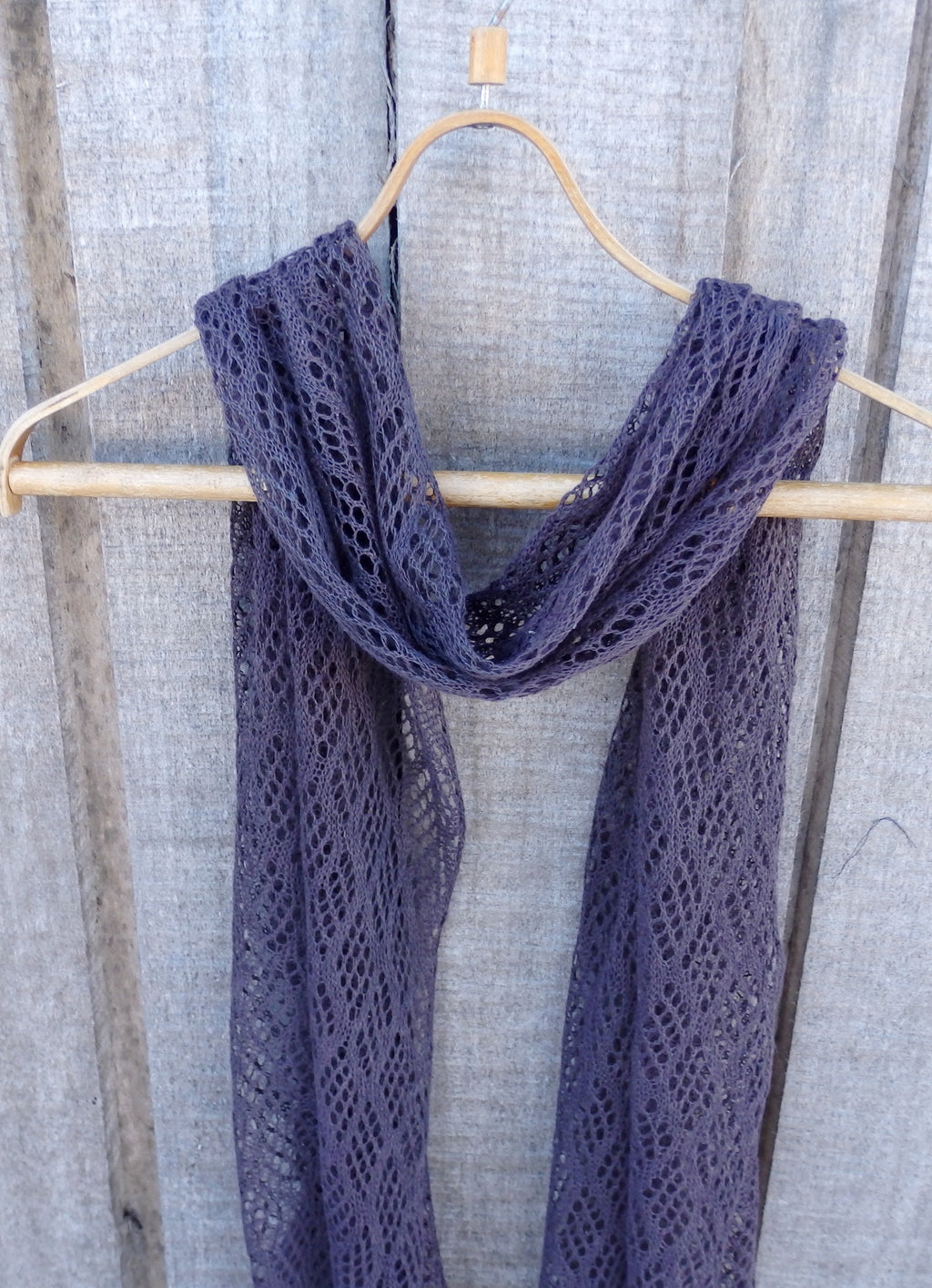 Purple lace scarf hanging on a wooden hanger against a textured gray background