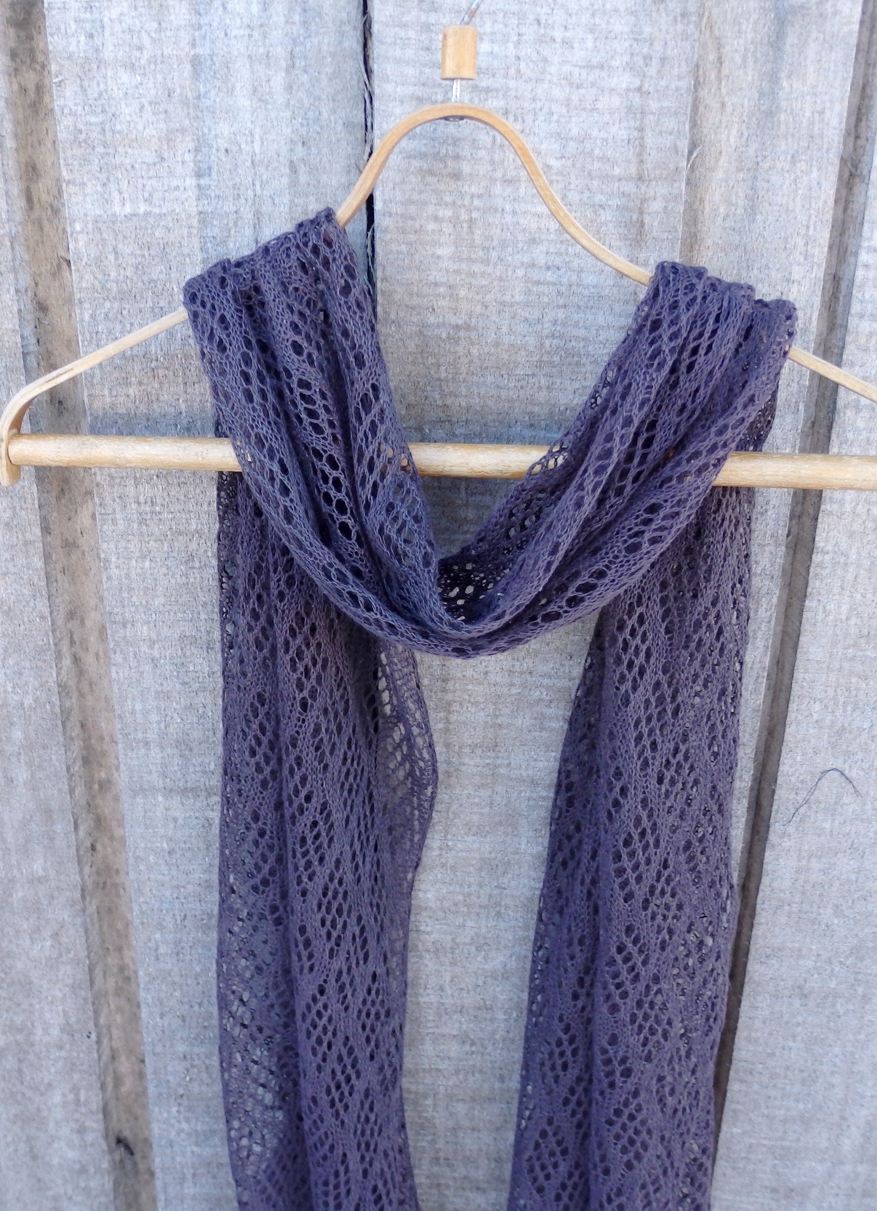 Purple lace scarf hanging on a wooden hanger against a textured gray background