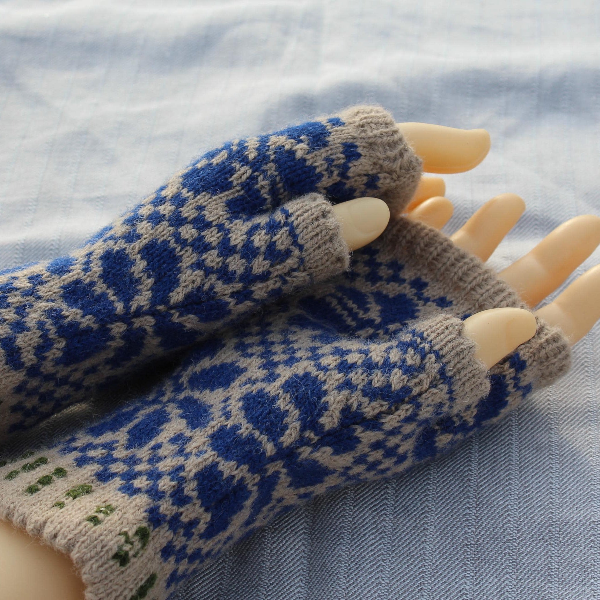 Pair of blue and beige patterned fingerless gloves on a mannequin hand against a light fabric background.
