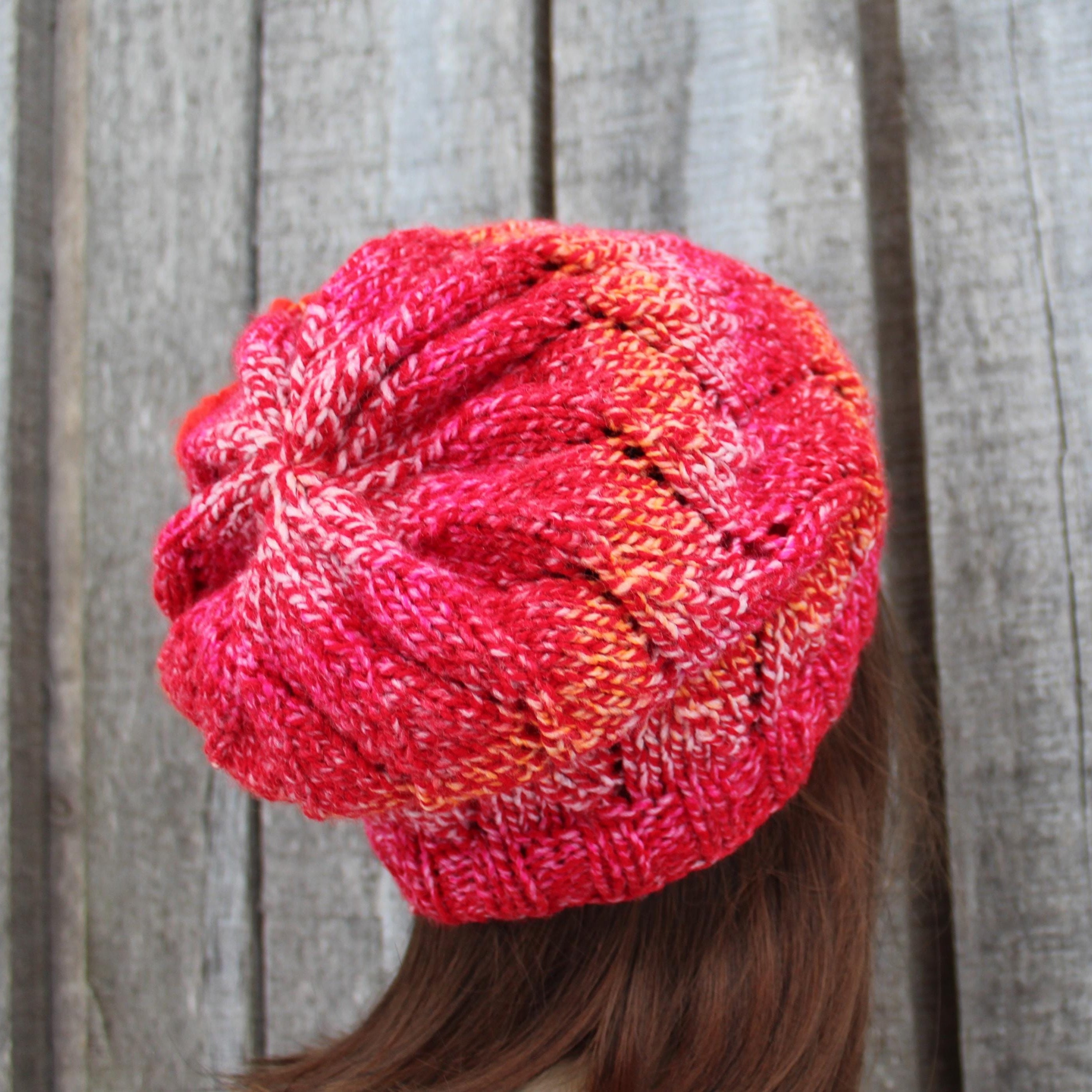 Pink knitted beanie worn by a person against a wooden fence background
