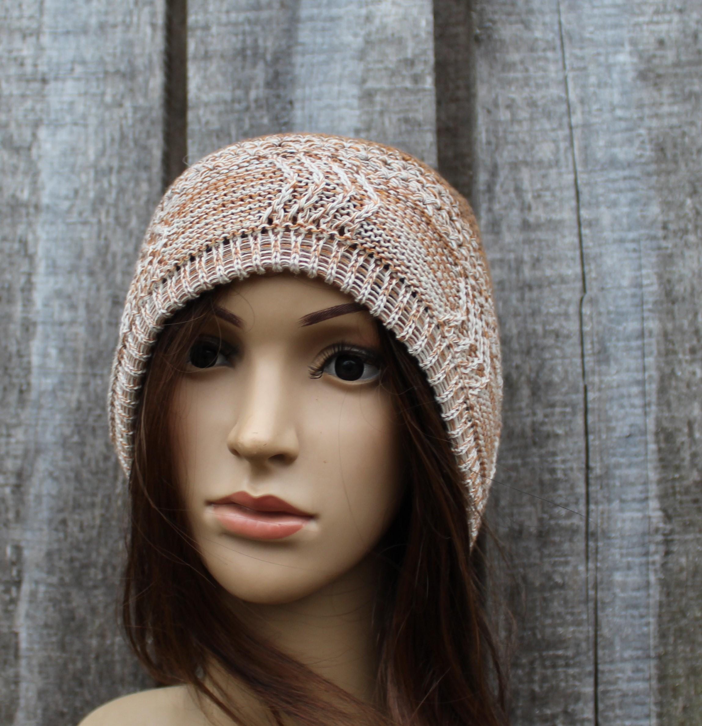 Knitted beige hat on a mannequin head against a textured gray background