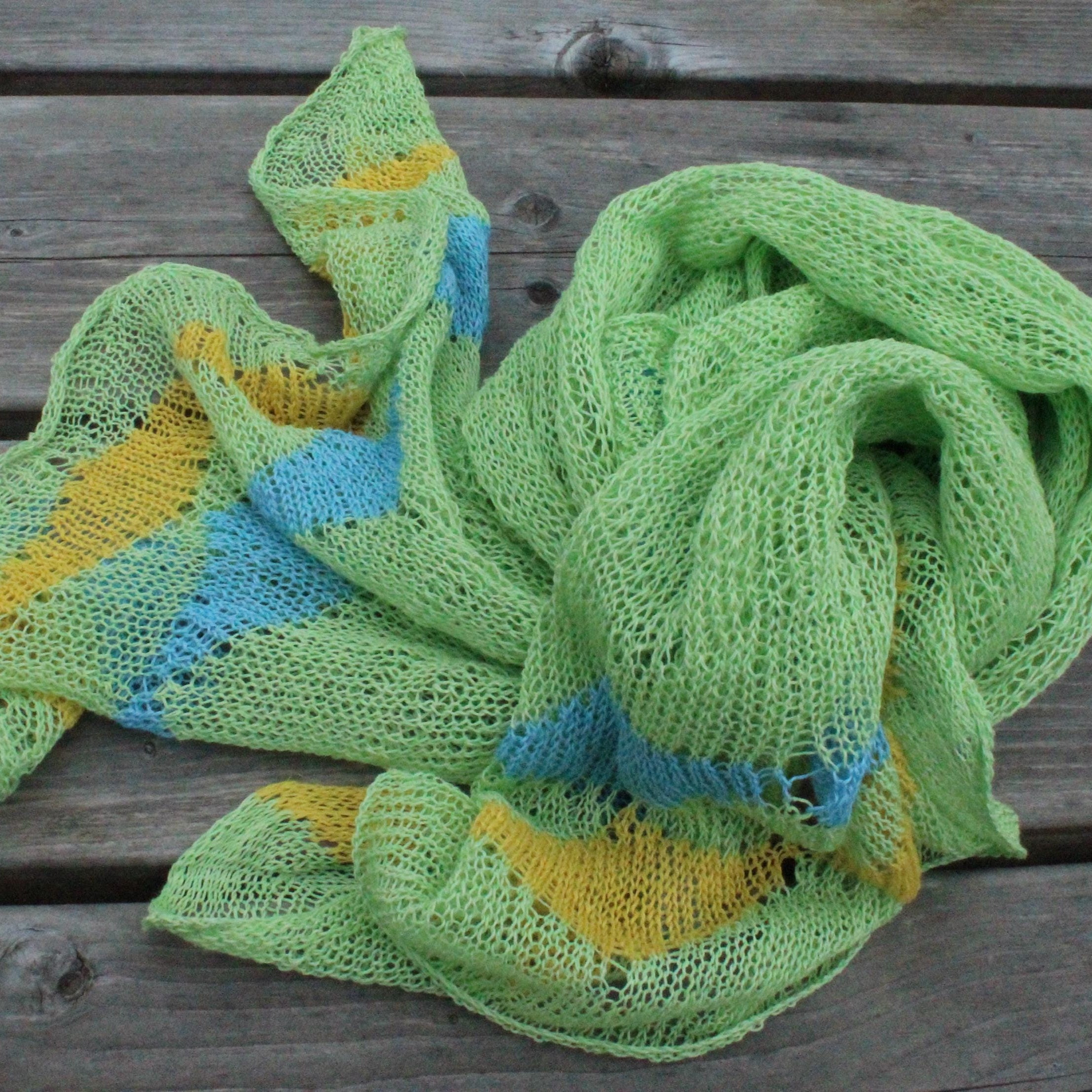 Green knitted scarf with blue and yellow patterns on a wooden surface