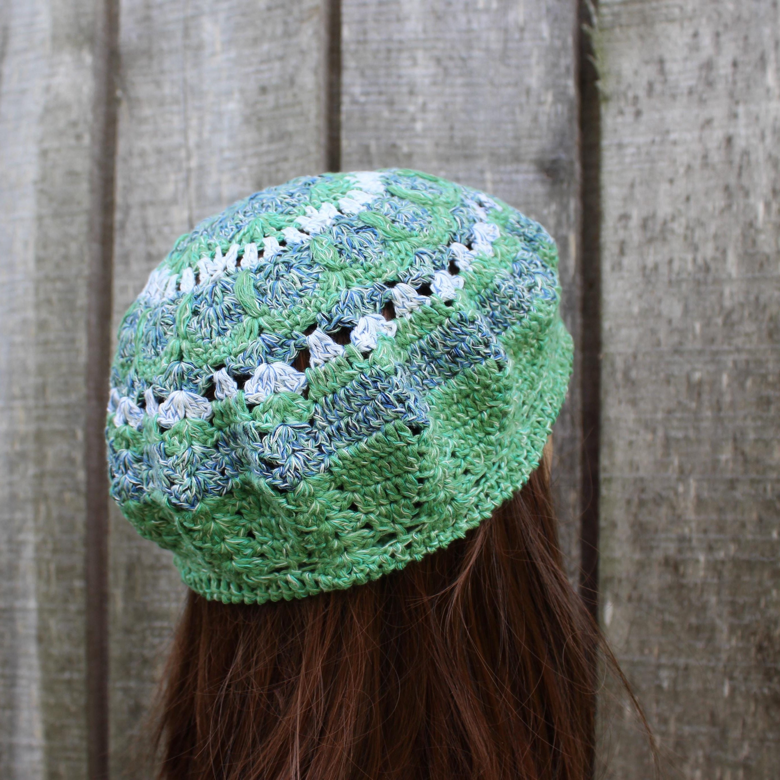 Green knitted hat with white patterns worn by a person against a wooden fence background