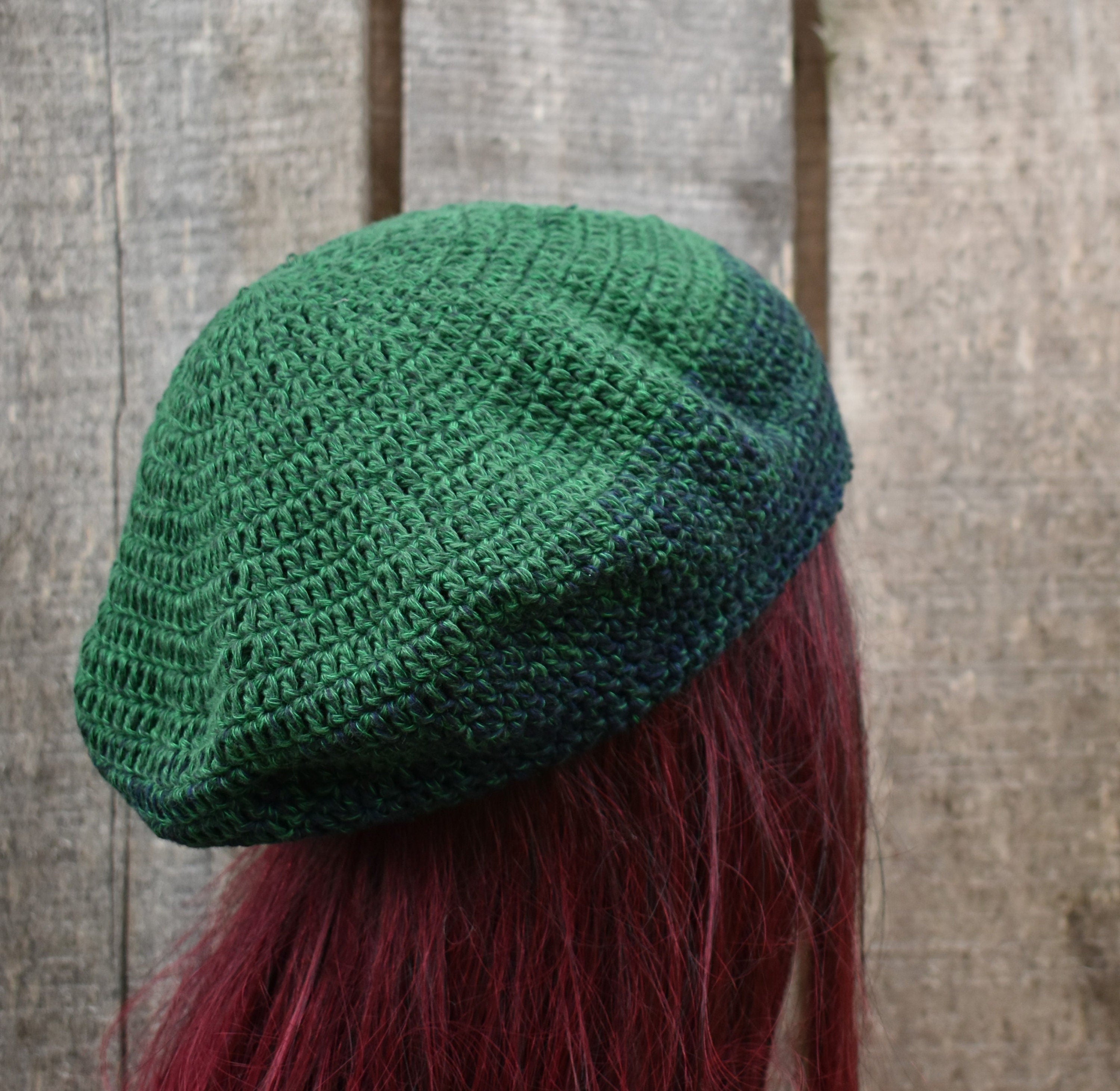 Green knitted beret worn by a person with red hair against a wooden background