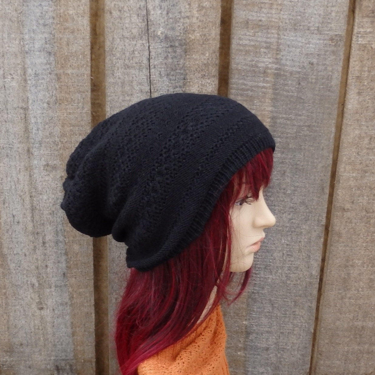 Mannequin head wearing a black knit beanie against a wooden panel background