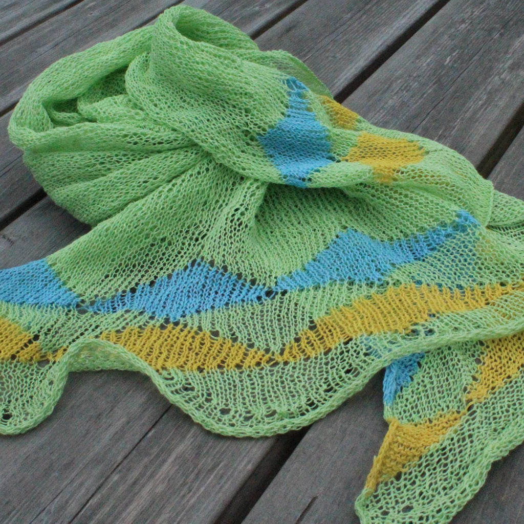 Green knitted scarf with blue and yellow patterns on a wooden surface