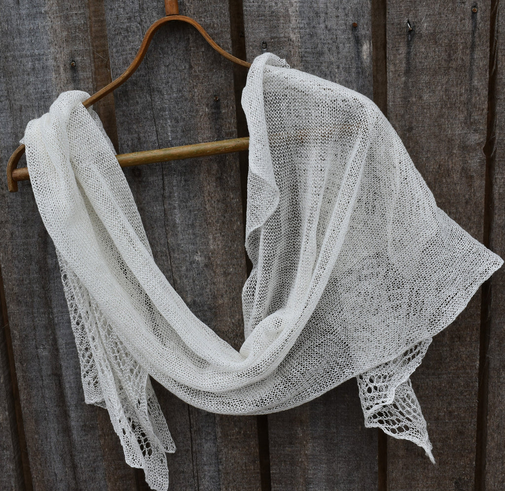 White lace shawl draped over a wooden hanger against a rustic wooden background