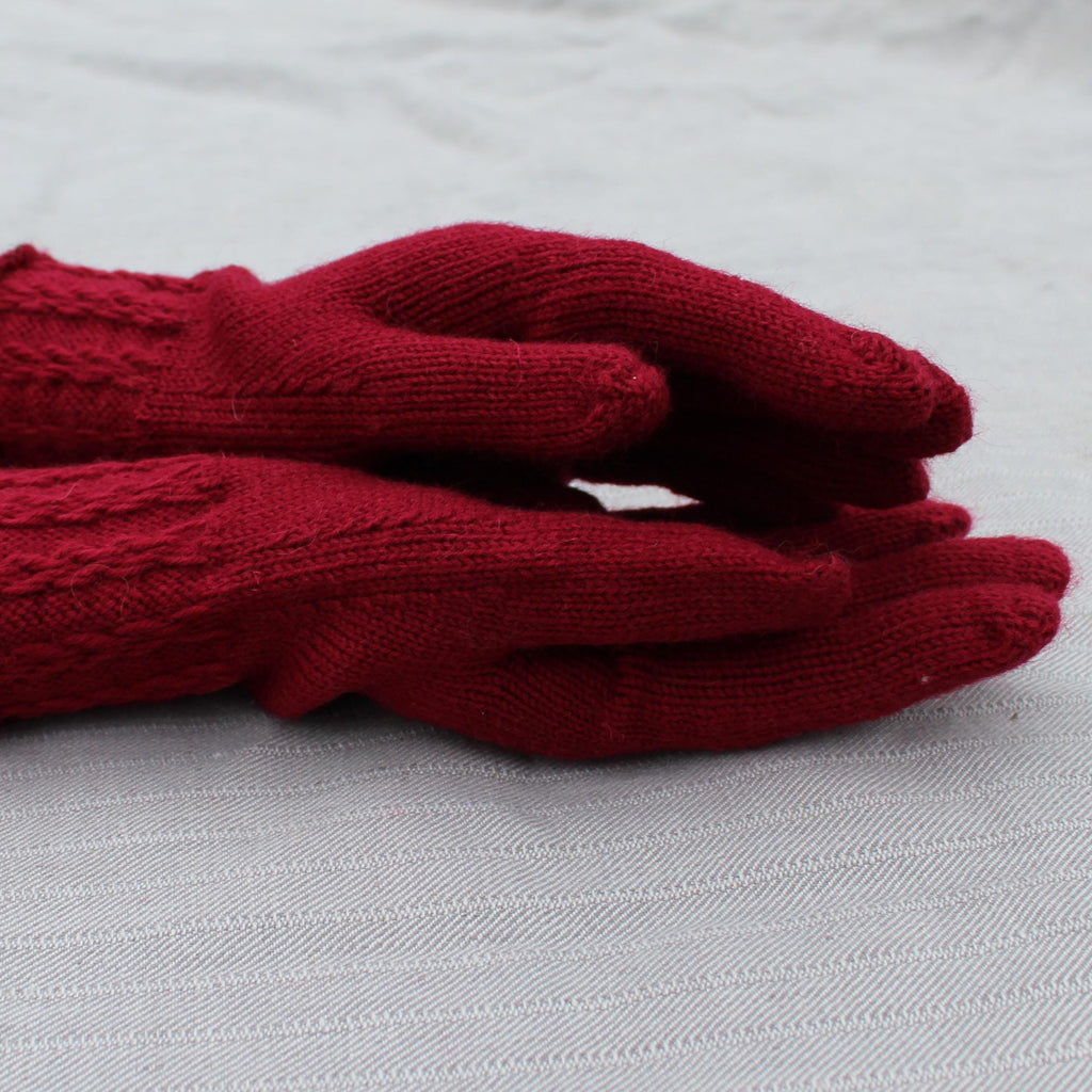 Pair of red knitted gloves on a light gray surface