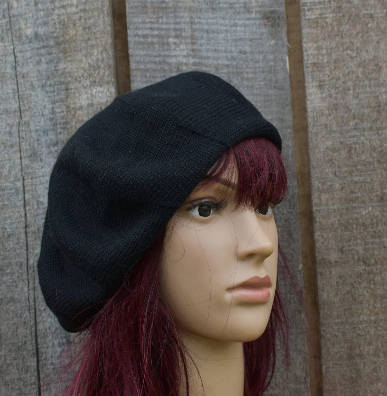 Black beret on a mannequin head with red hair against a wooden background
