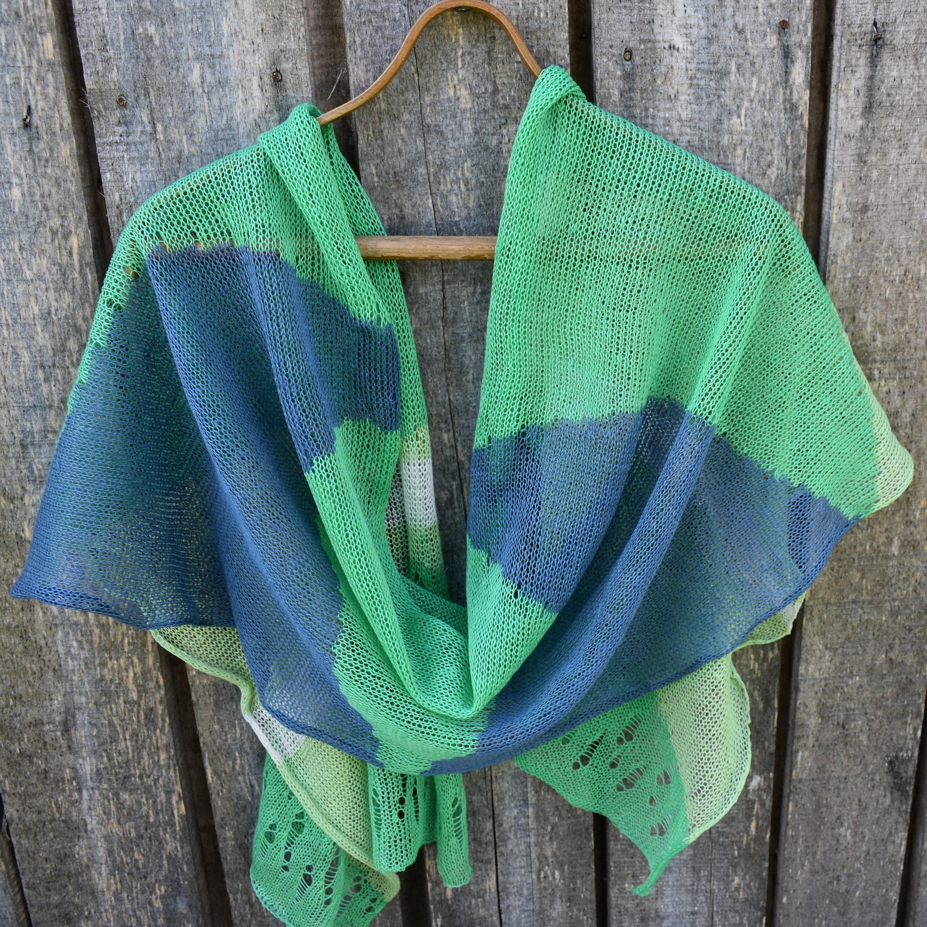 Green and blue knitted shawl on a wooden hanger against a wooden background