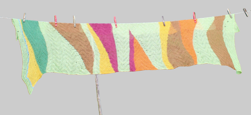 Colorful knitted blanket hanging on a clothesline outdoors with greenery in the background