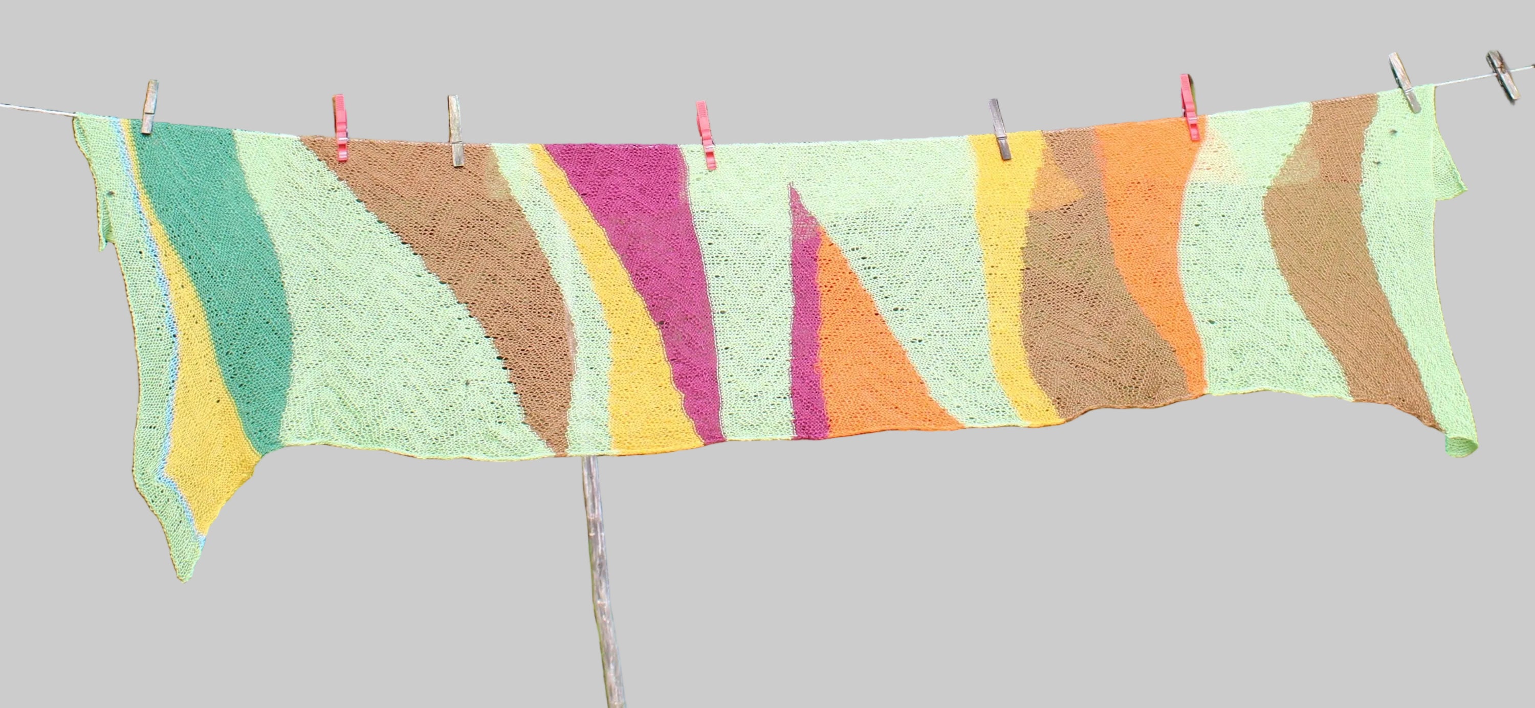 Colorful knitted blanket hanging on a clothesline outdoors with greenery in the background