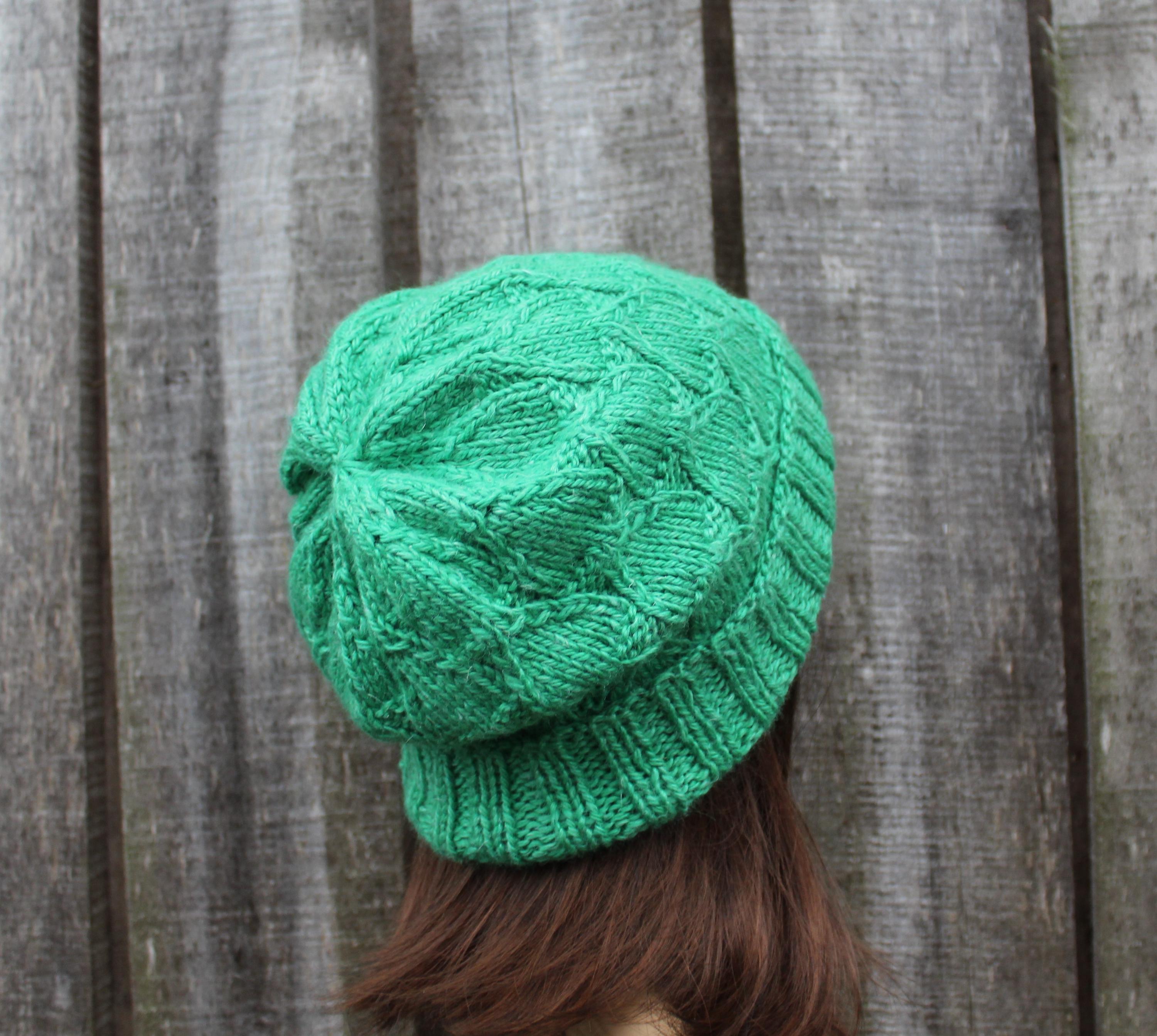Green knitted beanie worn by a person against a wooden background