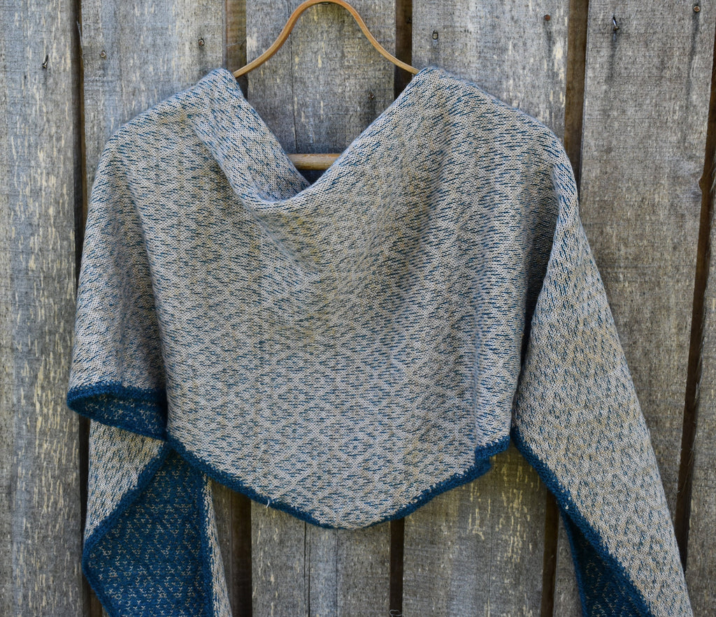Gray and blue knitted shawl on a wooden hanger against a wooden background