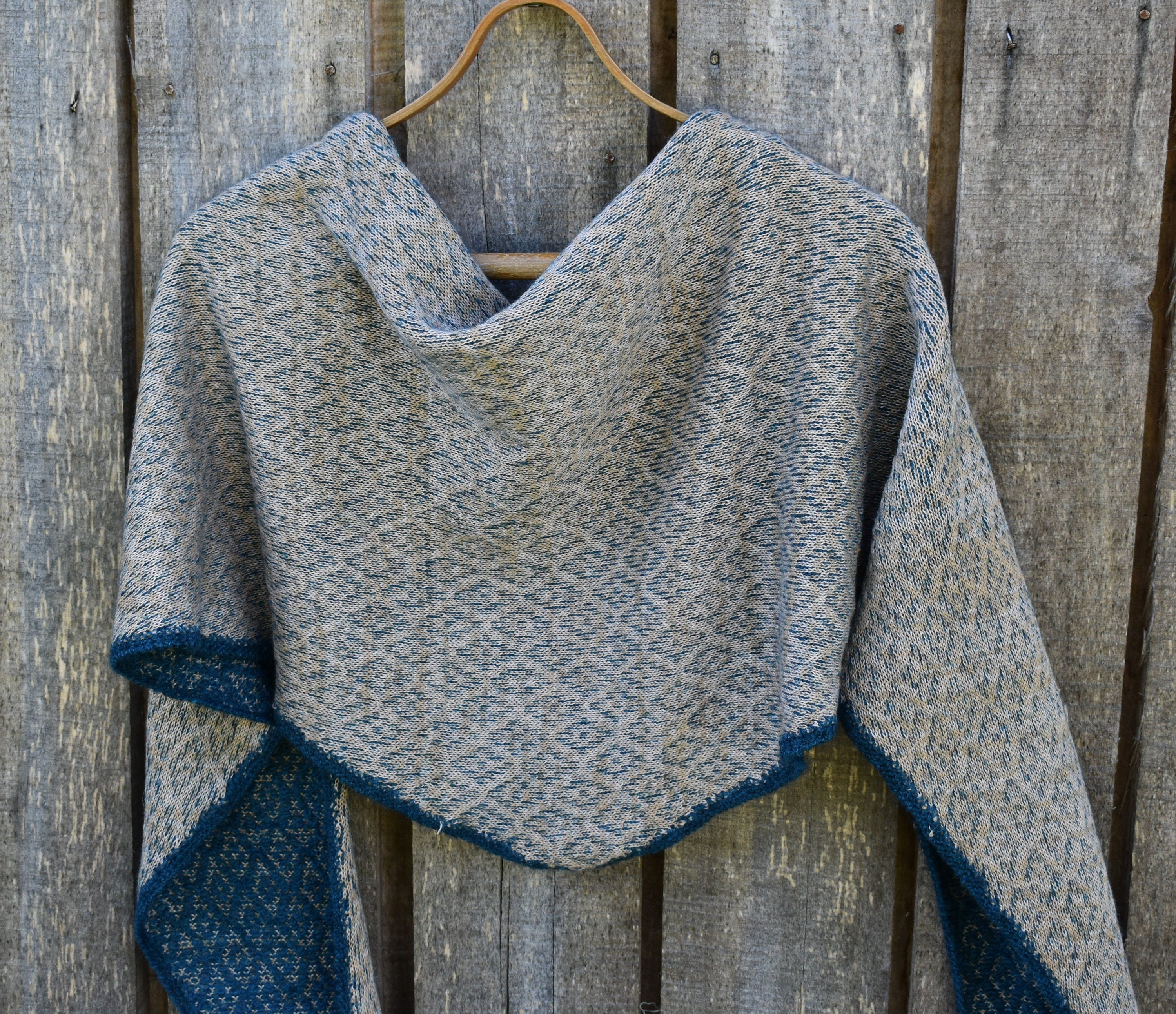 Gray and blue knitted shawl on a wooden hanger against a wooden background