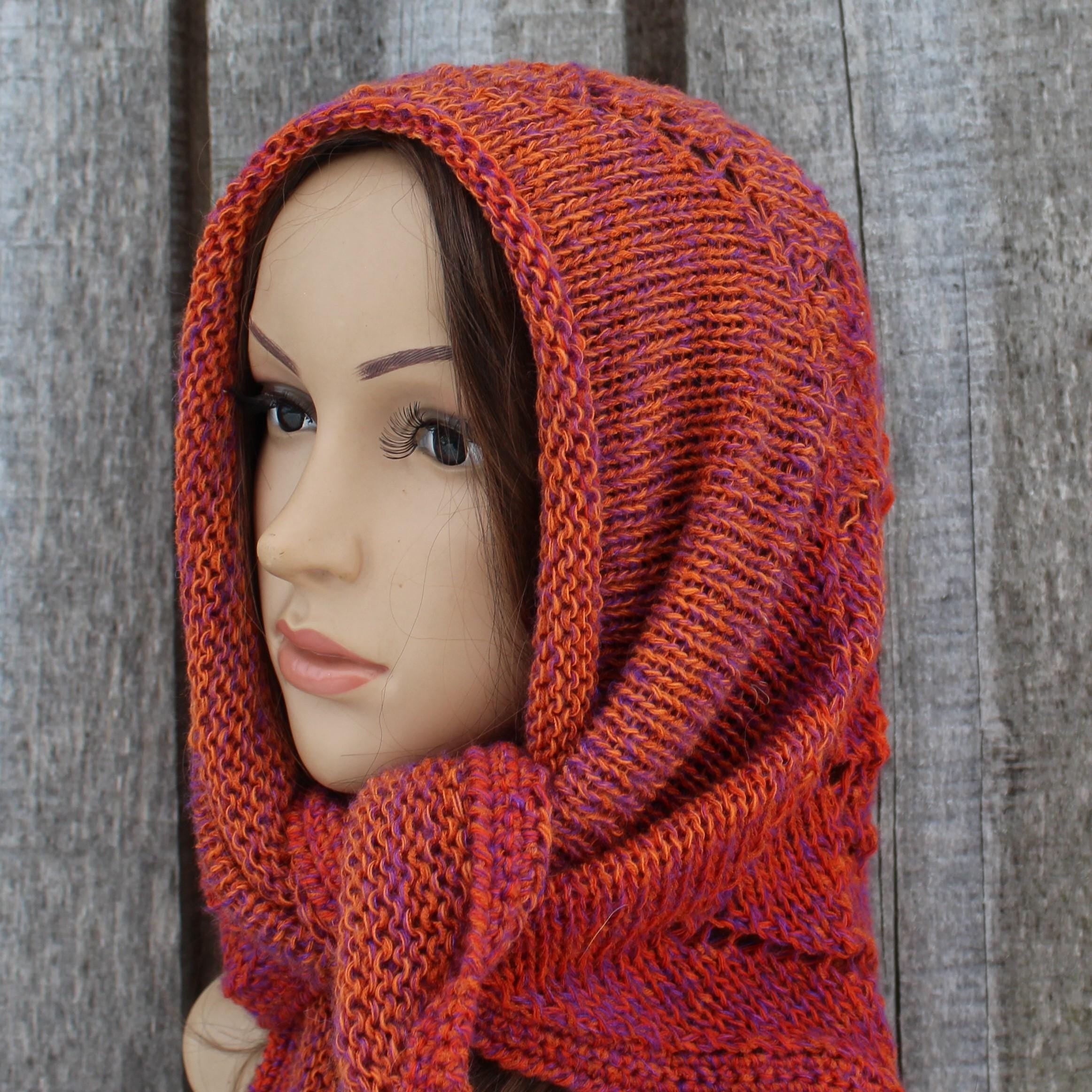 Mannequin head wearing a knitted orange and purple scarf against a wooden background