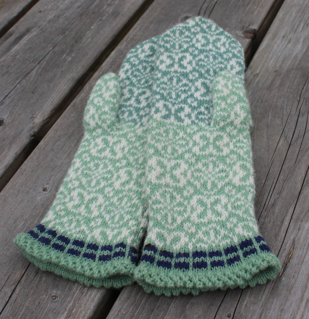 Green and white patterned knitted gloves on a wooden surface