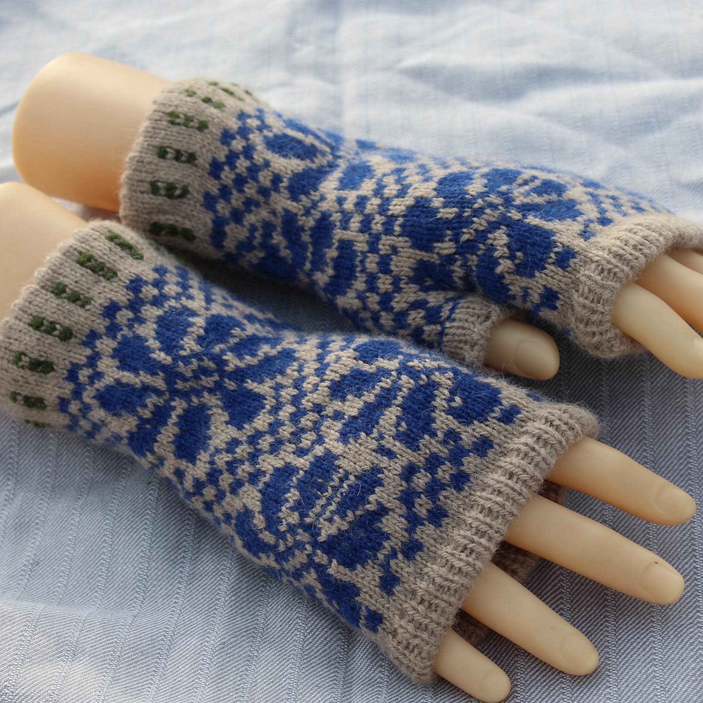 Pair of blue and beige patterned fingerless gloves on a mannequin hand against a light fabric background.