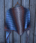 Knitted shawl with a geometric pattern draped over a wooden hanger against a wooden background