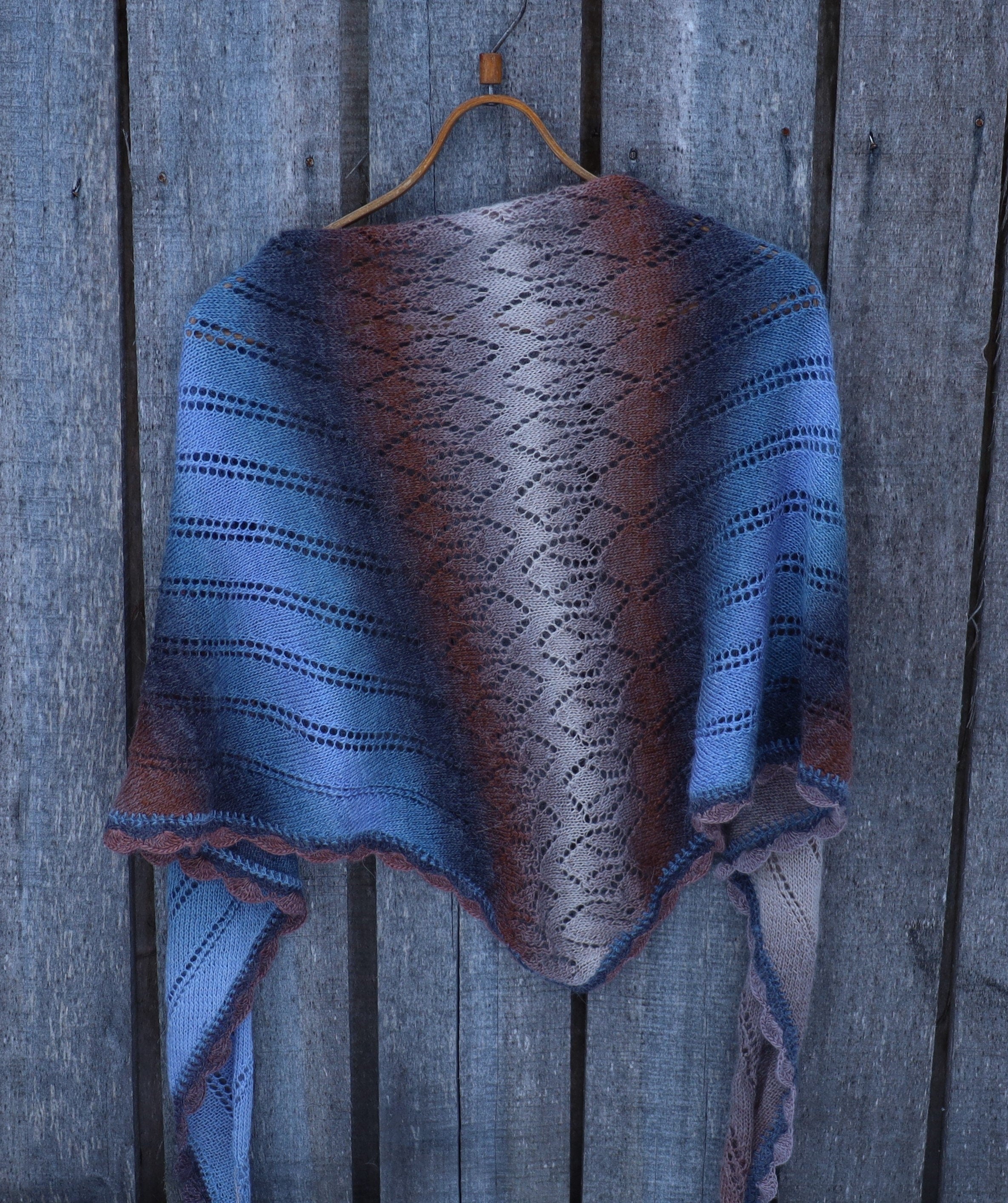 Knitted shawl with a geometric pattern draped over a wooden hanger against a wooden background