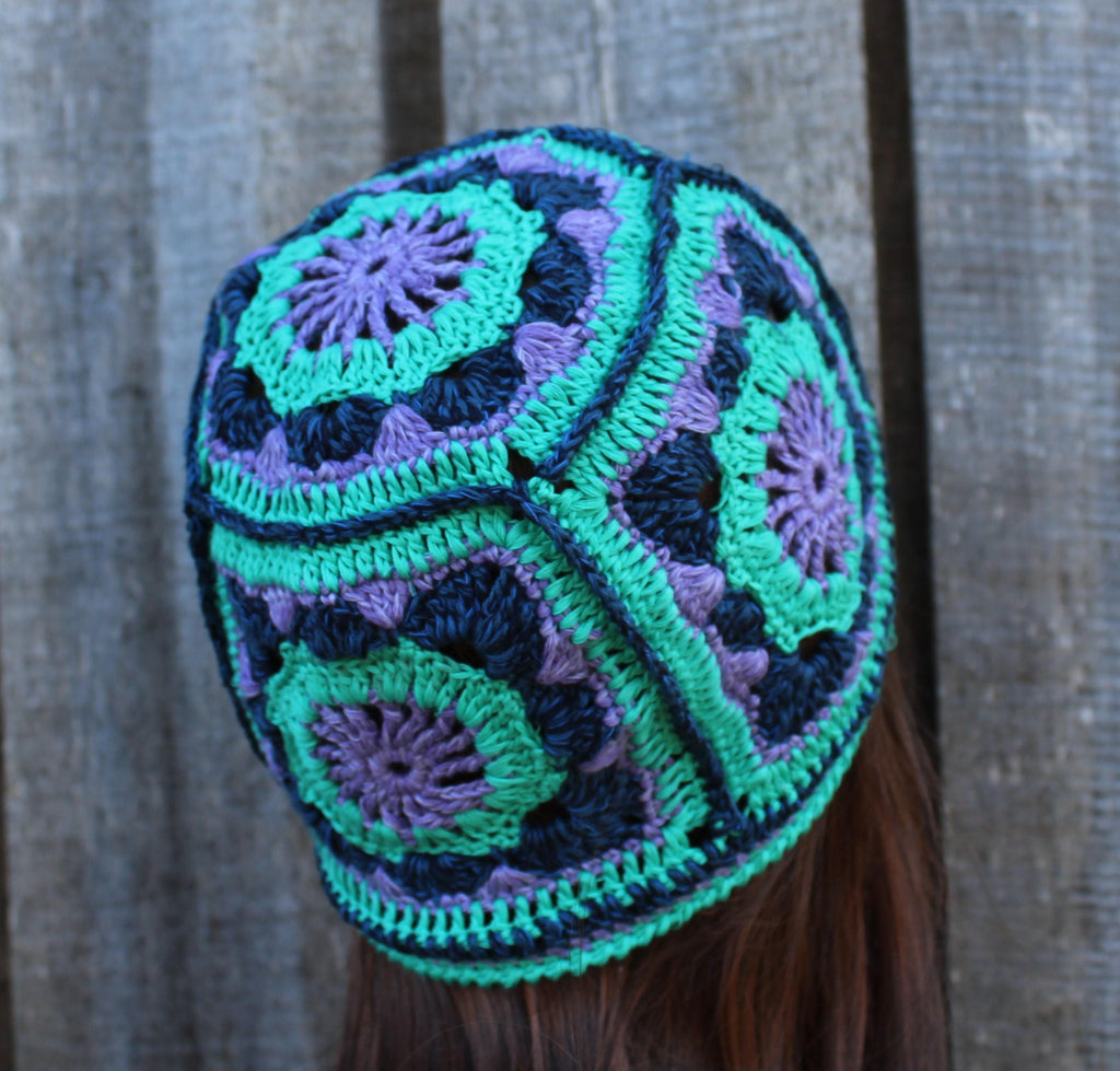 Colorful crocheted beanie with green and purple patterns against a wooden background