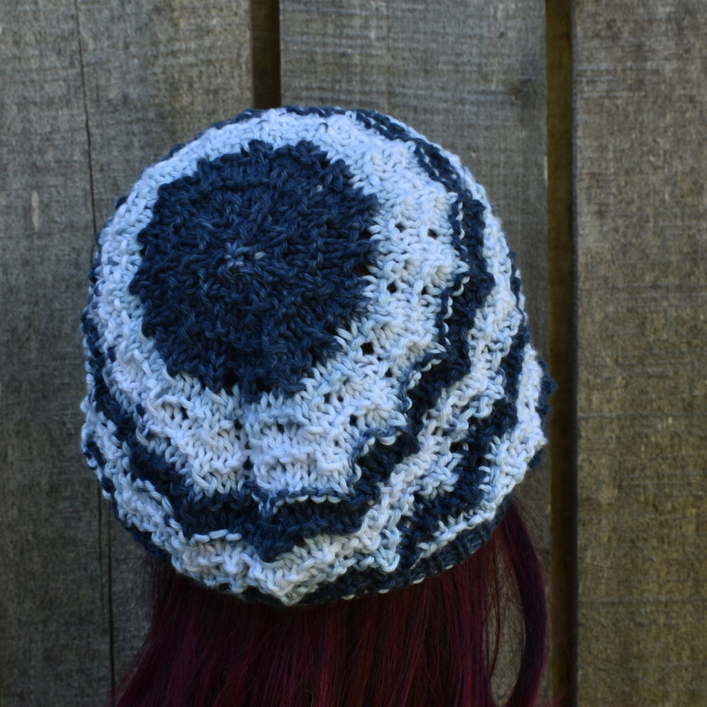 Blue and white crocheted beanie on a person with red hair against a wooden background