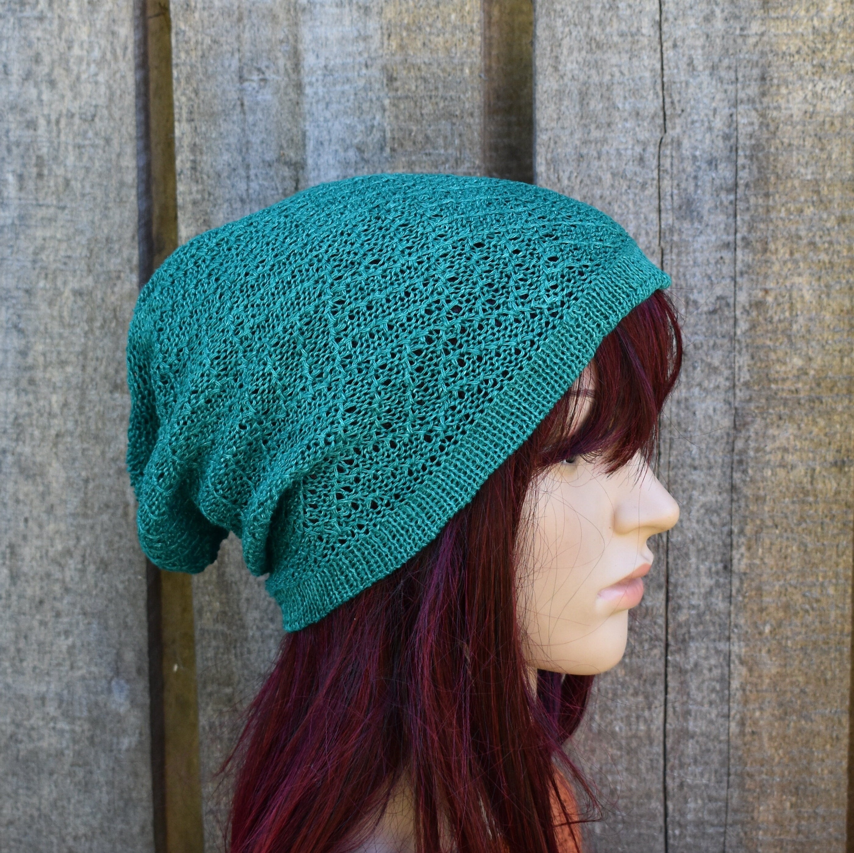 Teal knitted beanie worn by a person with red hair against a wooden background