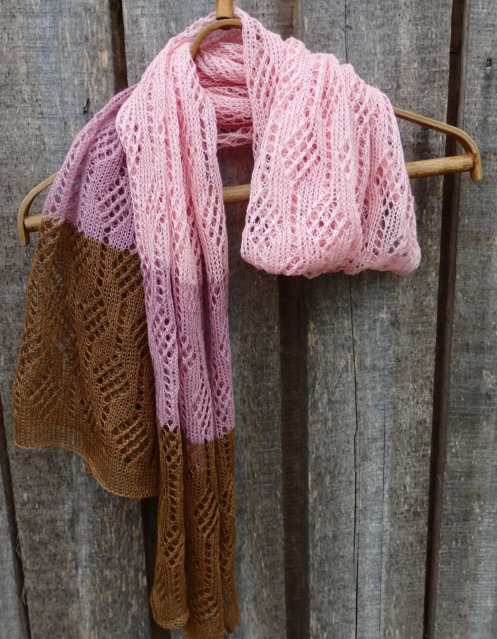 Two knitted scarves, one pink and one brown, hanging on a wooden rod against a wooden background.