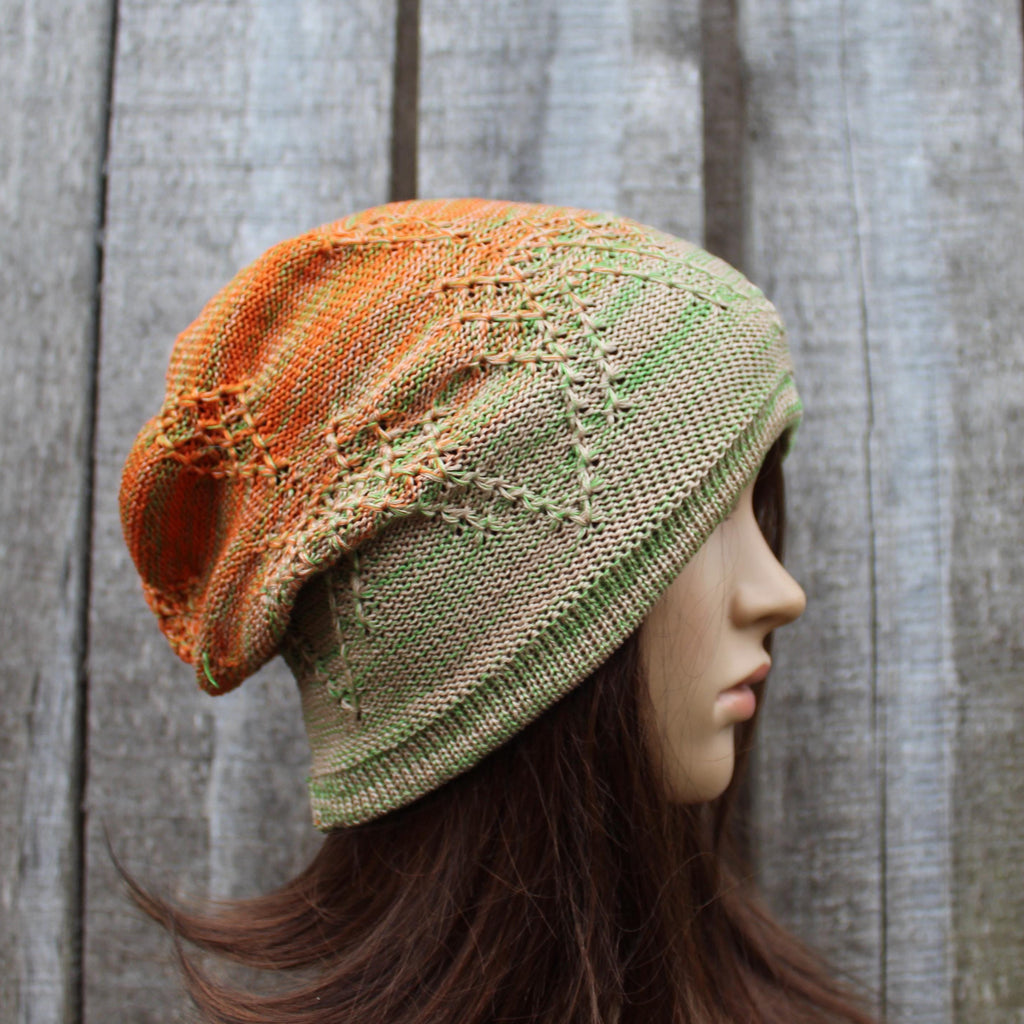 Knitted hat with orange and green gradient on a mannequin head against a wooden background