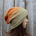 Knitted hat with orange and green gradient on a mannequin head against a wooden background