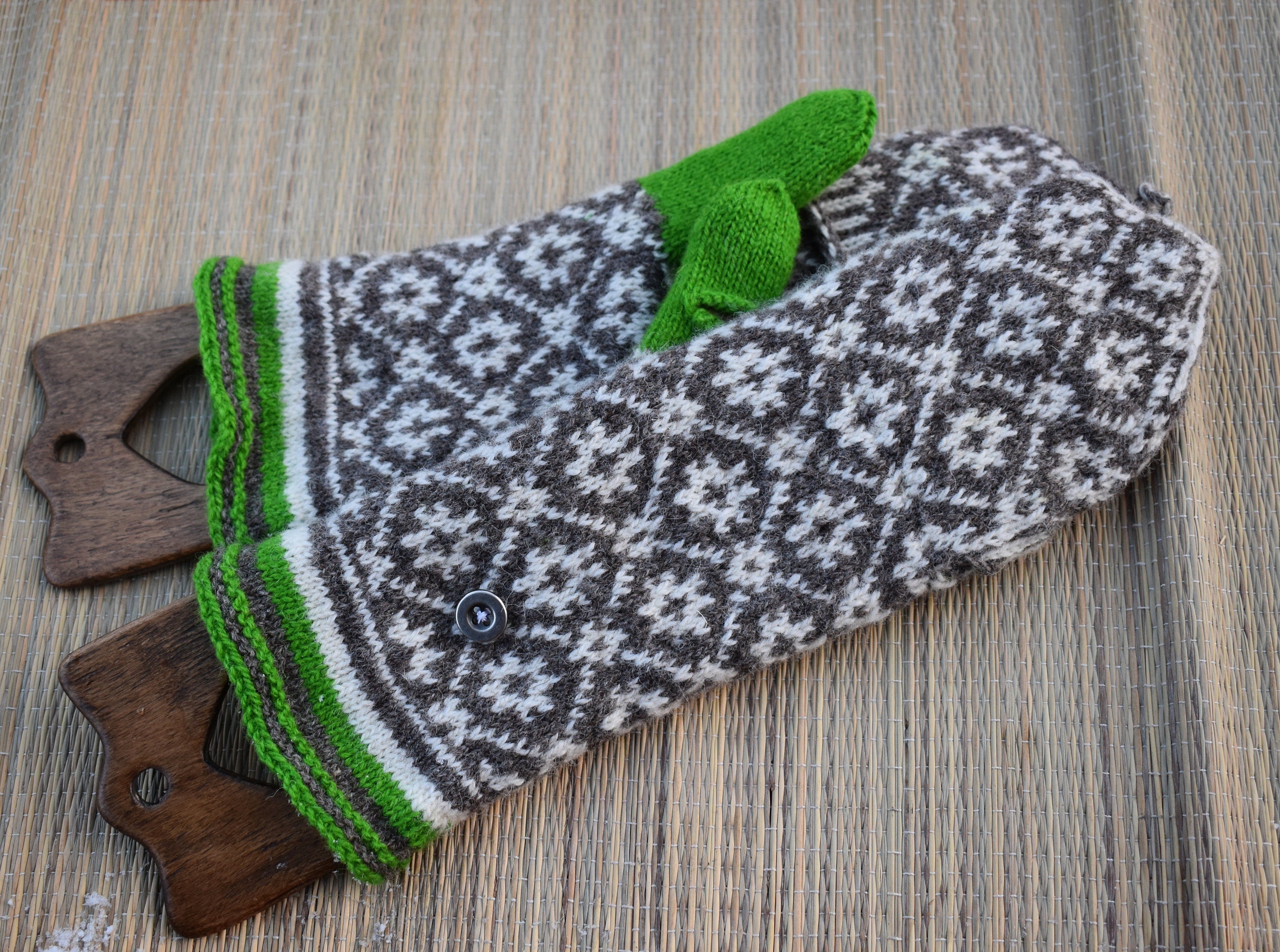 Pair of patterned mittens with green trim on a wooden surface